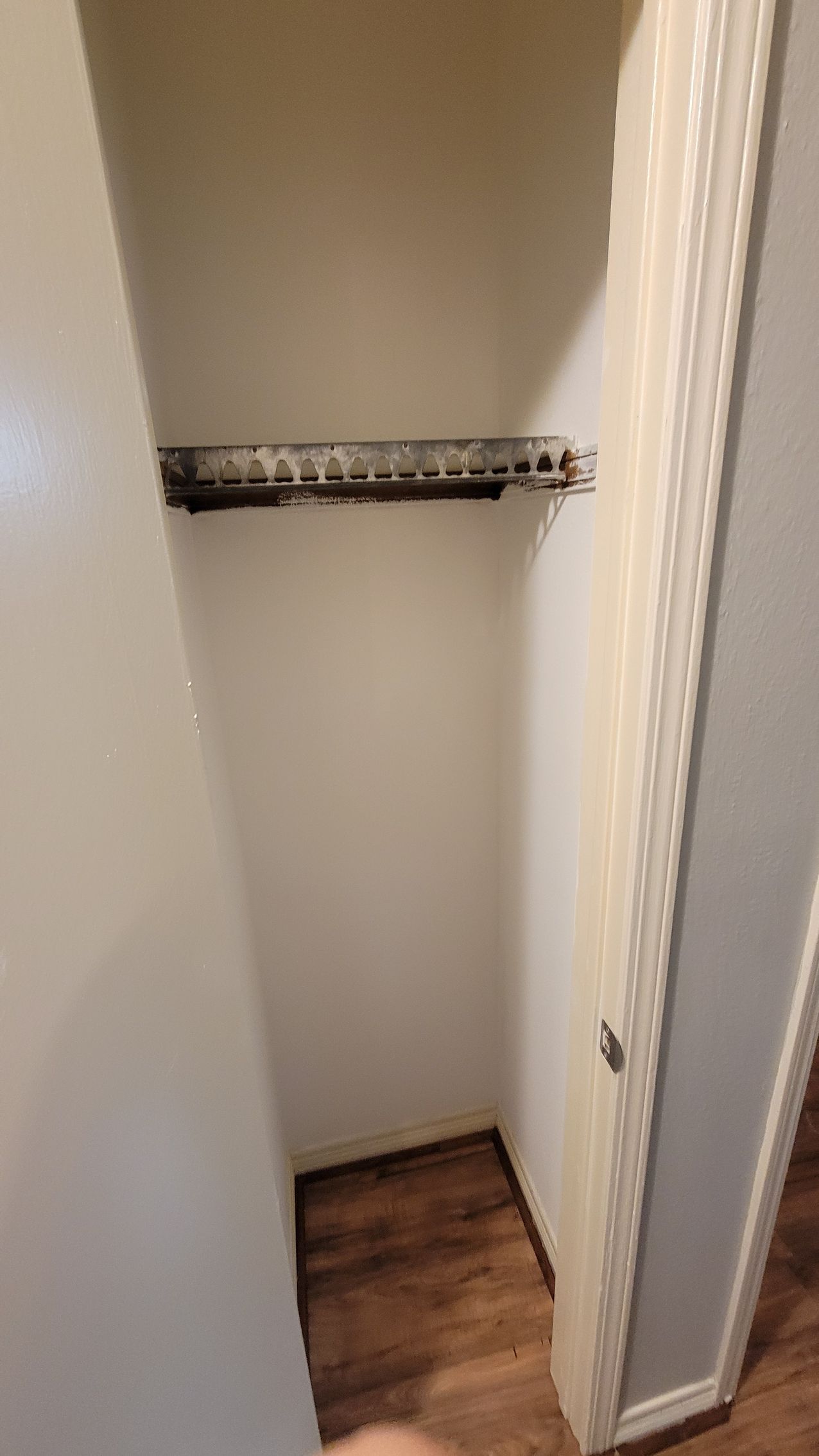 Empty white closet with a wire shelf, brown floor, and a partially open door.