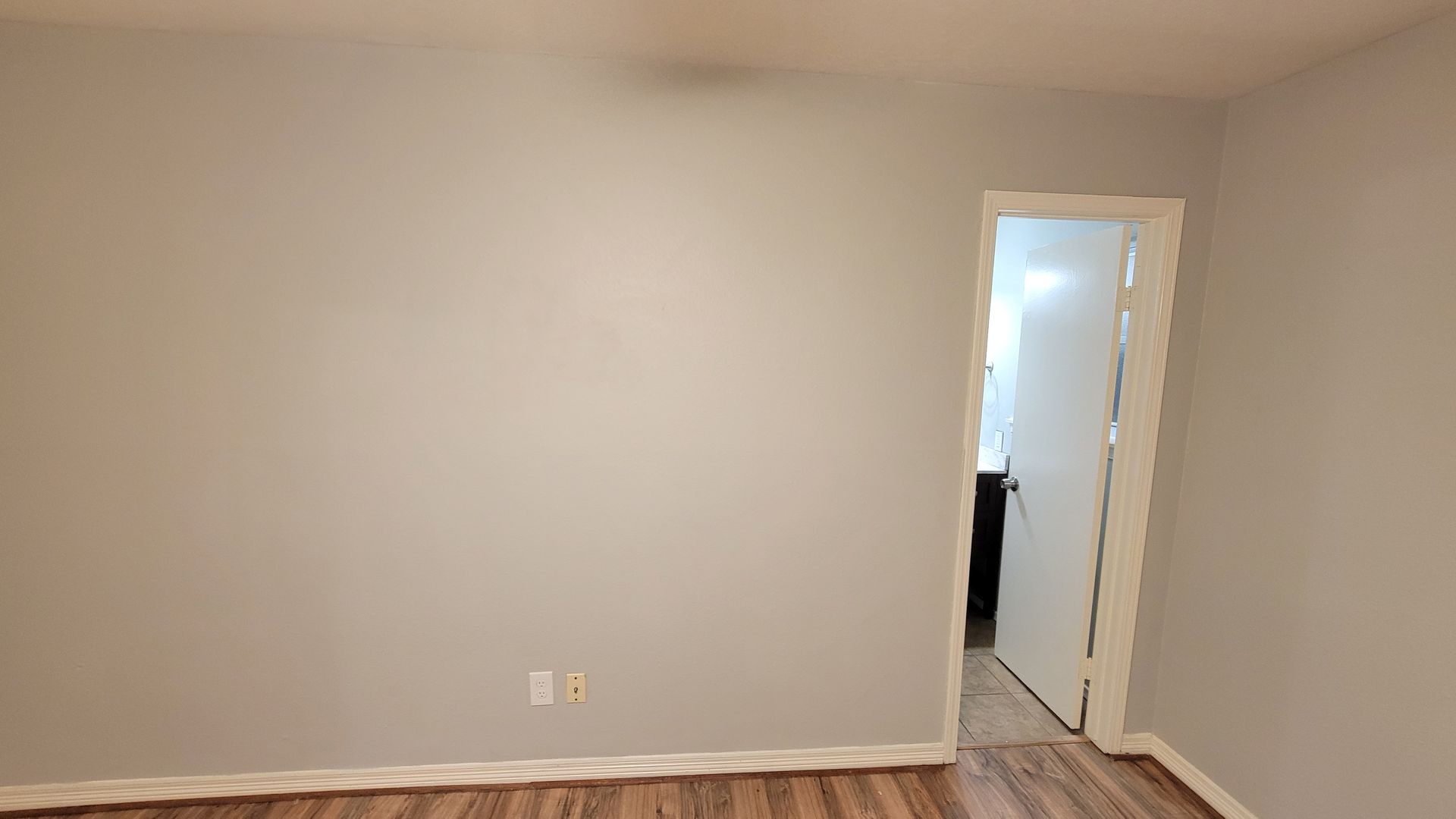 Empty room with gray walls, doorway, and wood-look flooring.