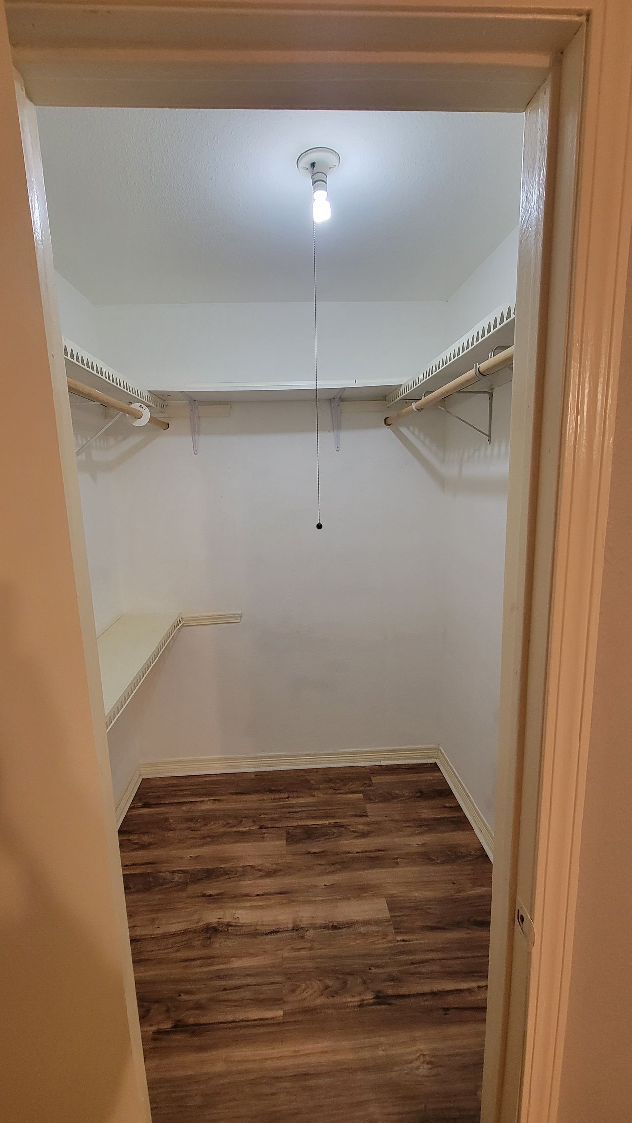 Empty walk-in closet with shelves and wood-look flooring, light hanging from ceiling.