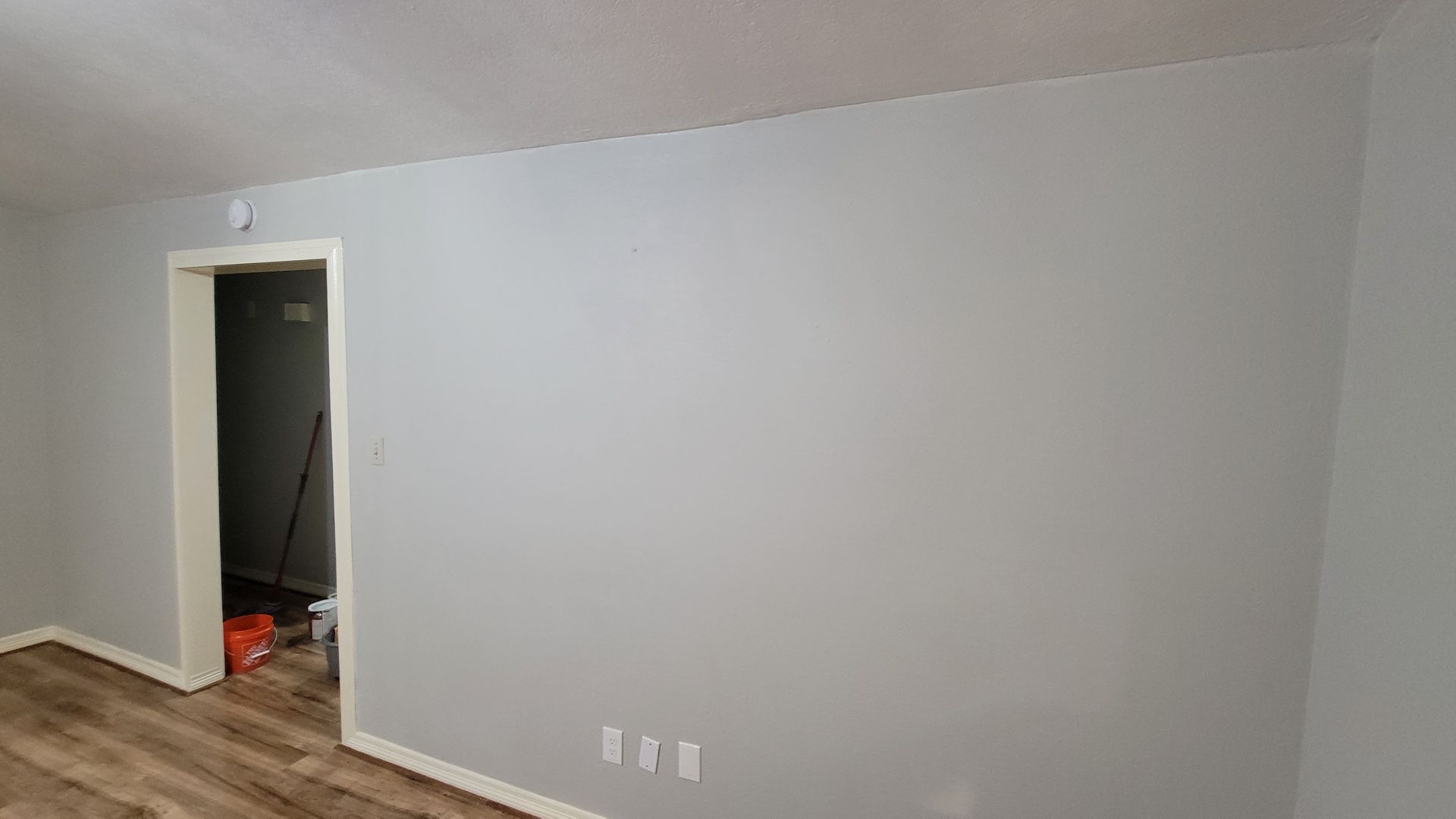 Empty room with gray walls, white ceiling, and wood-look flooring. A doorway leads to another room.