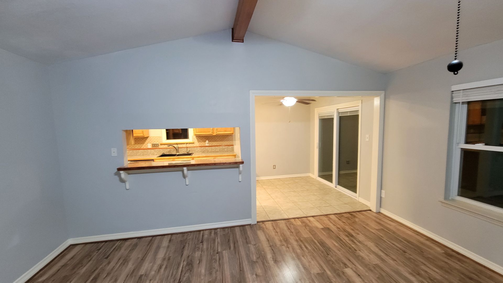 Interior view of a living space with gray walls, wood-look flooring, and an opening to the kitchen.