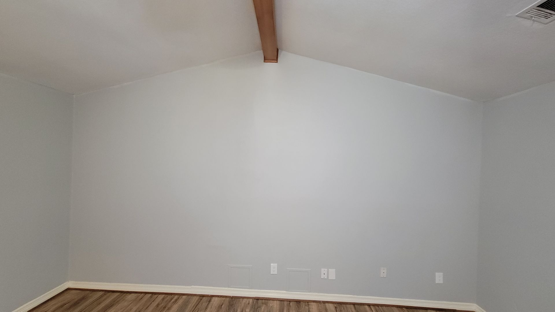 Empty room with light blue walls, a wood beam, and wood-look flooring.