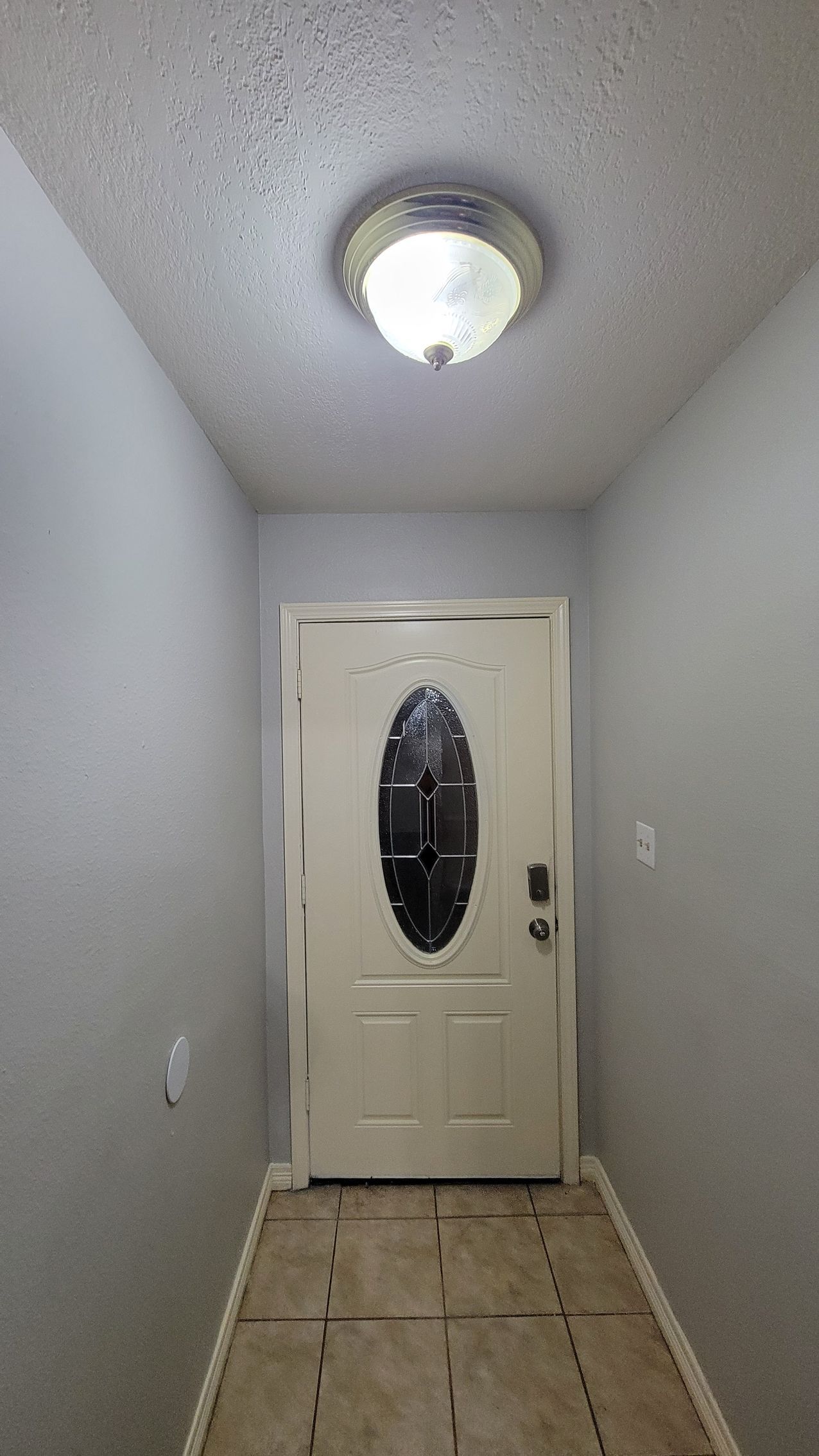 Hallway with gray walls, white door with oval window, and ceiling light.
