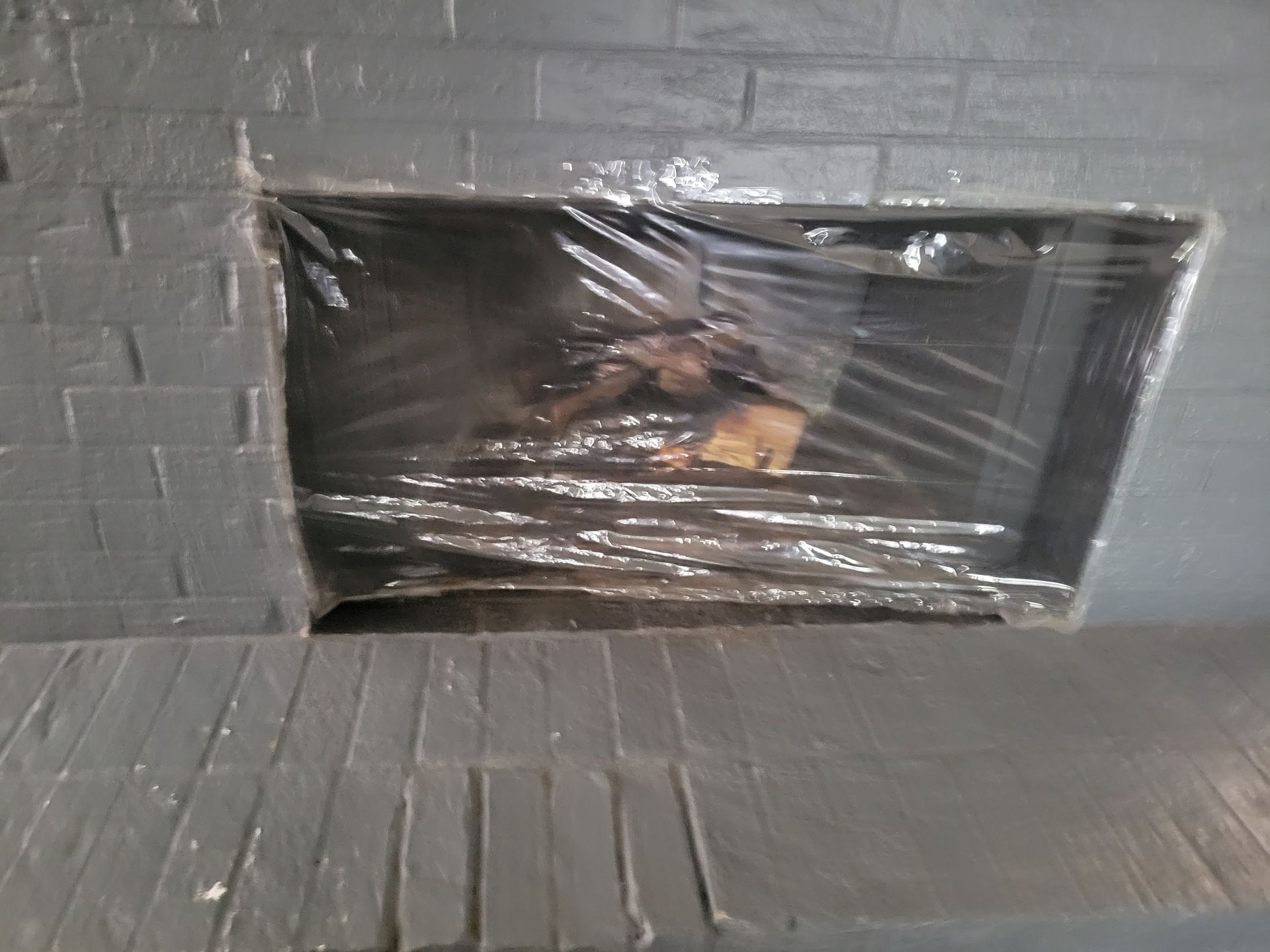 Fireplace wrapped in plastic, with painted gray brick surround.