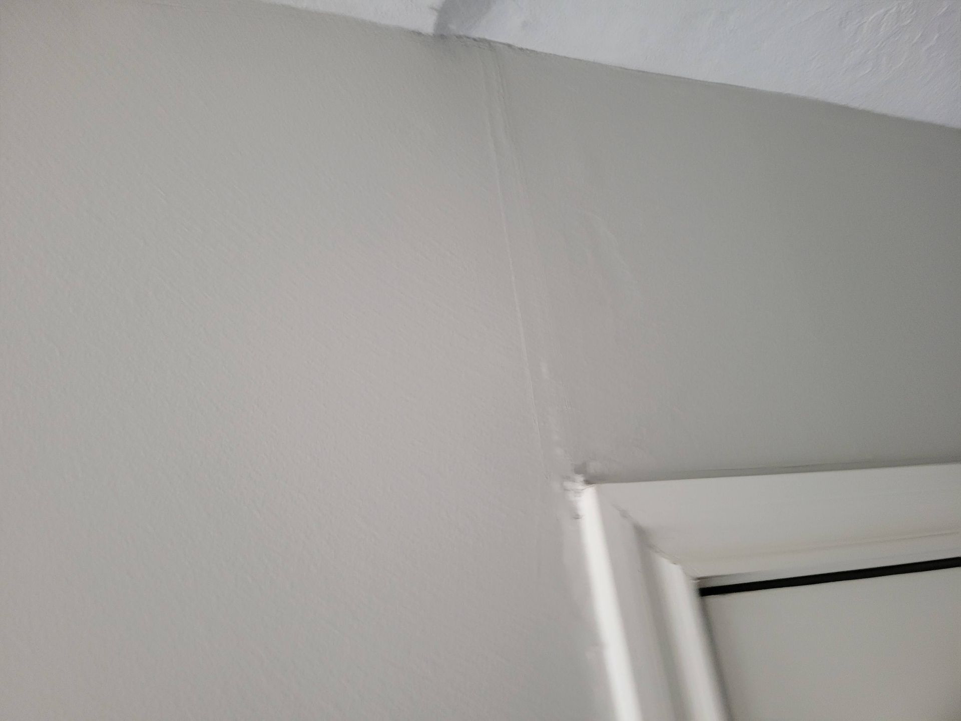 Light gray painted wall with a vertical crack, a white door frame, and white ceiling trim.