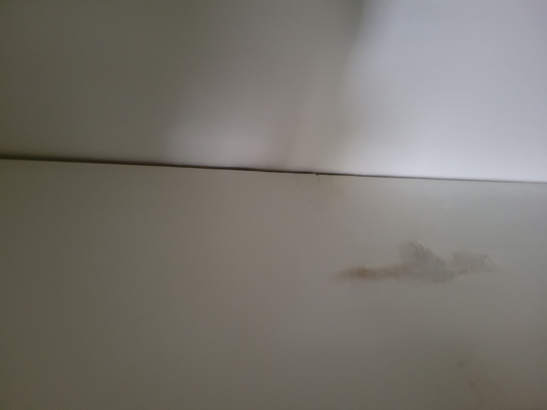 White wall with a brown stain and a seam, appears to be a ceiling.