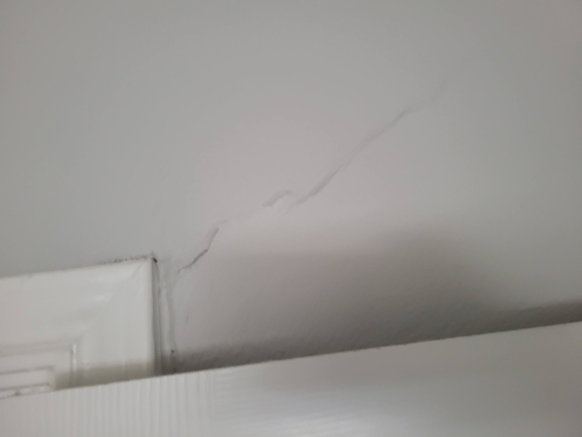 Crack in white ceiling above white door frame.