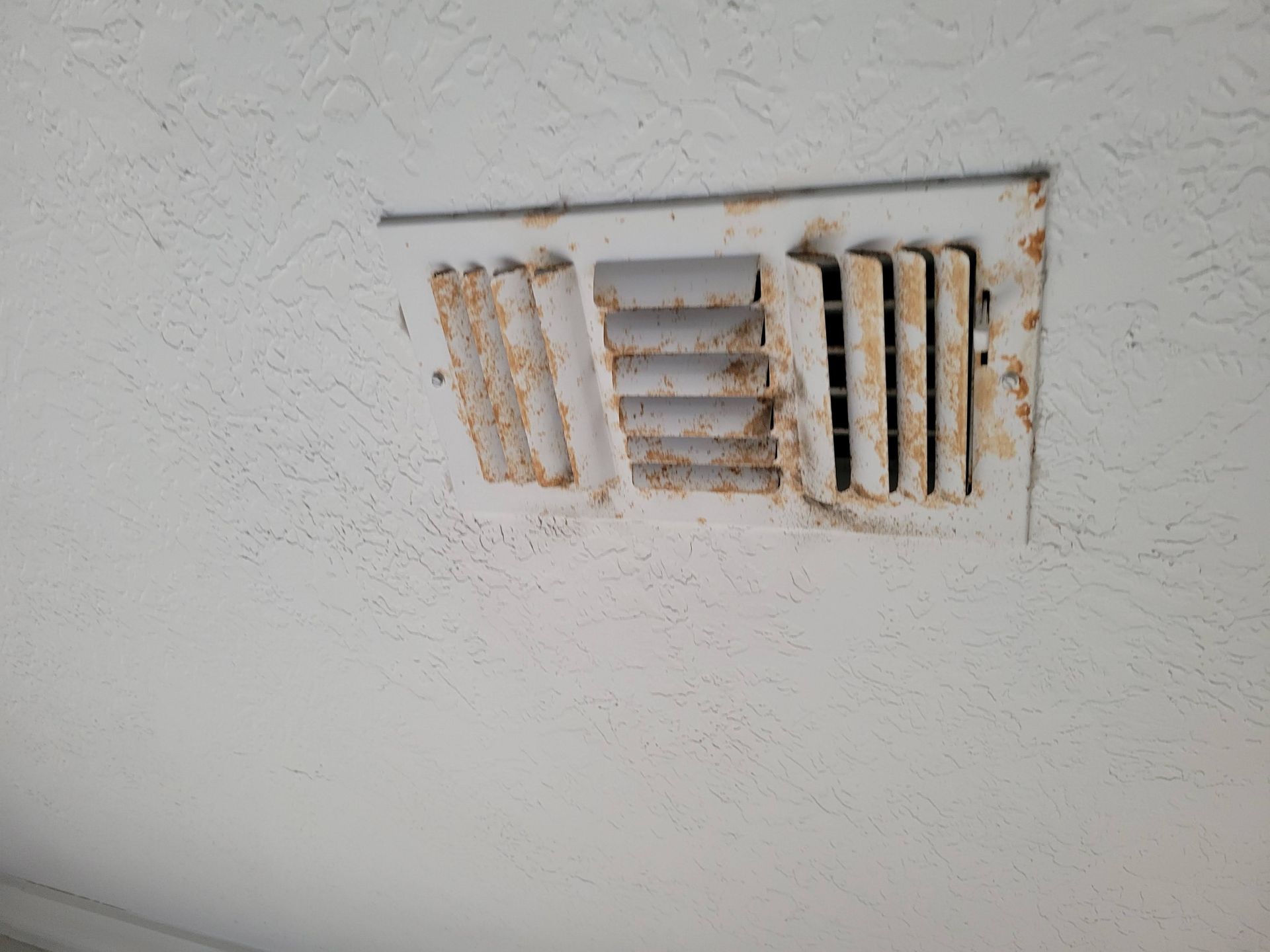 White, rusty air vent on a textured white wall.