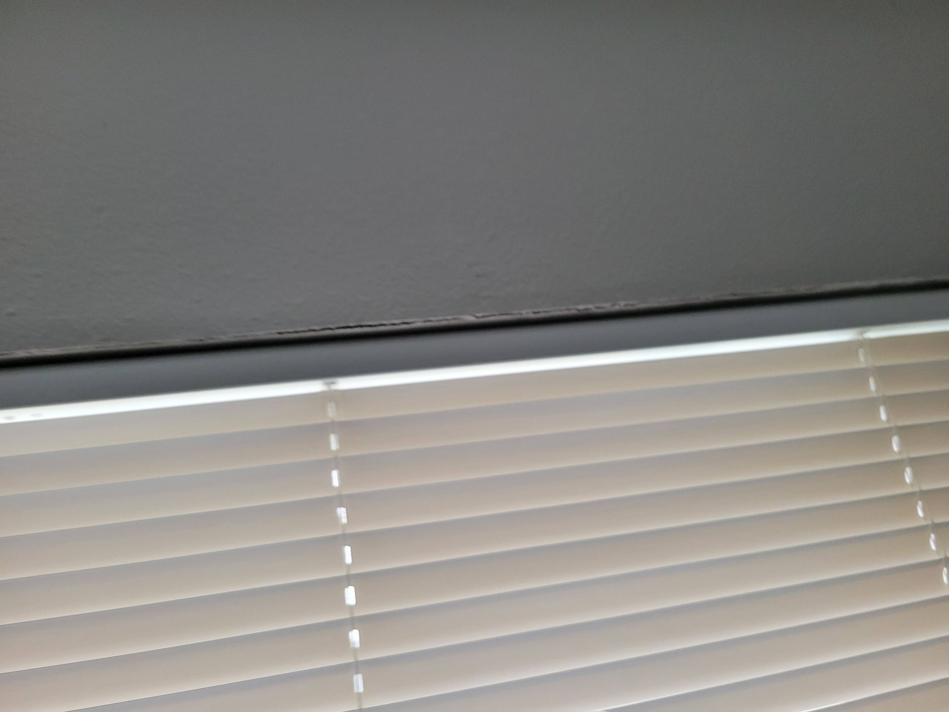 A close-up view of closed blinds and the corner of a gray ceiling.