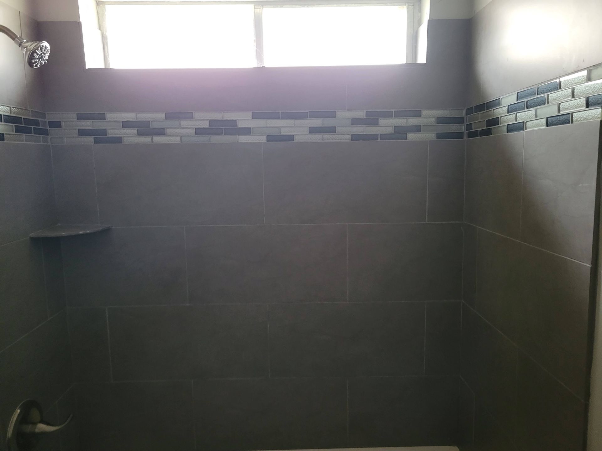 Dark tiled shower with a decorative mosaic tile border and a small shelf.
