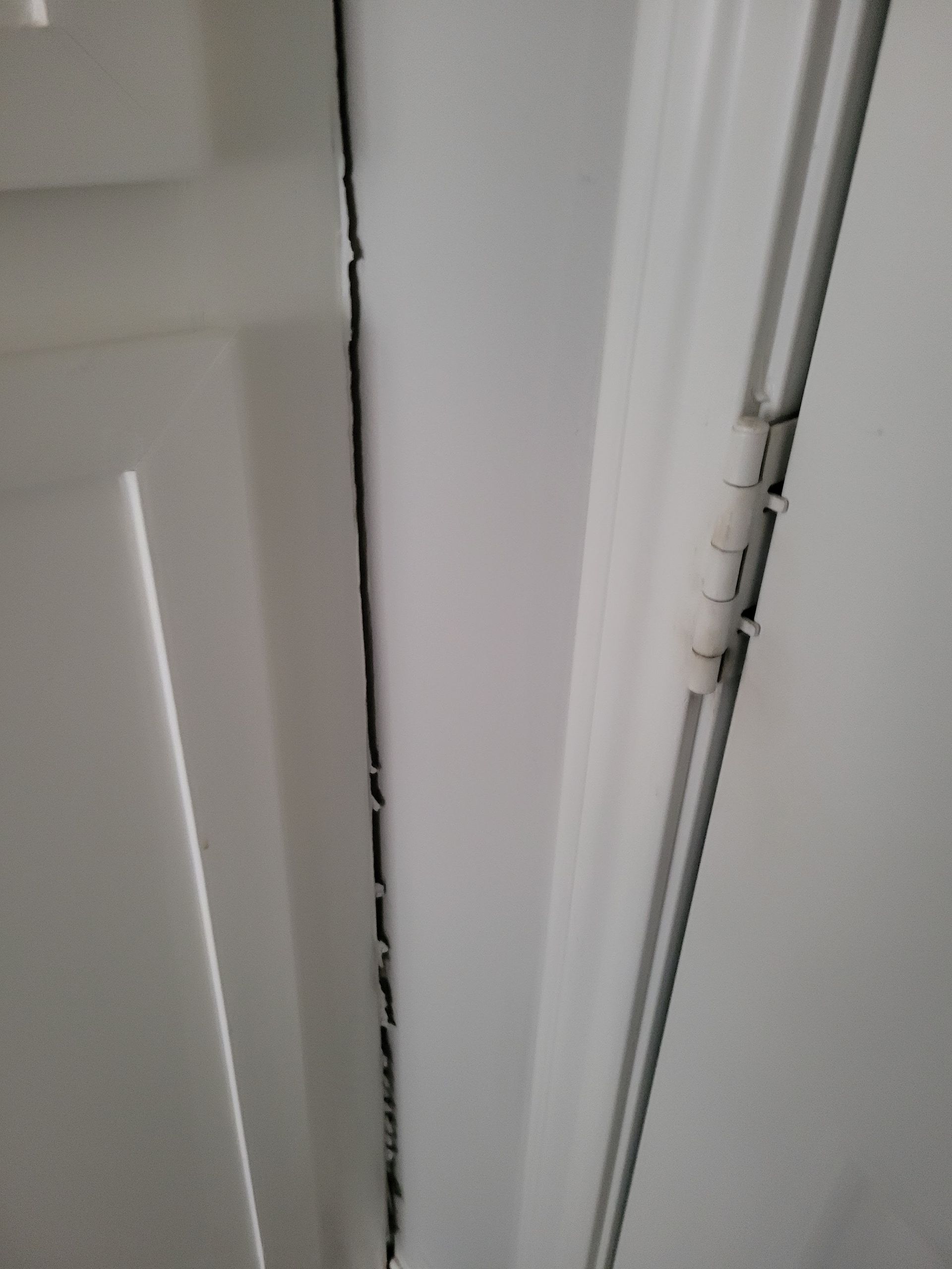 White door with a visible crack down the frame, with visible hinges on the right.