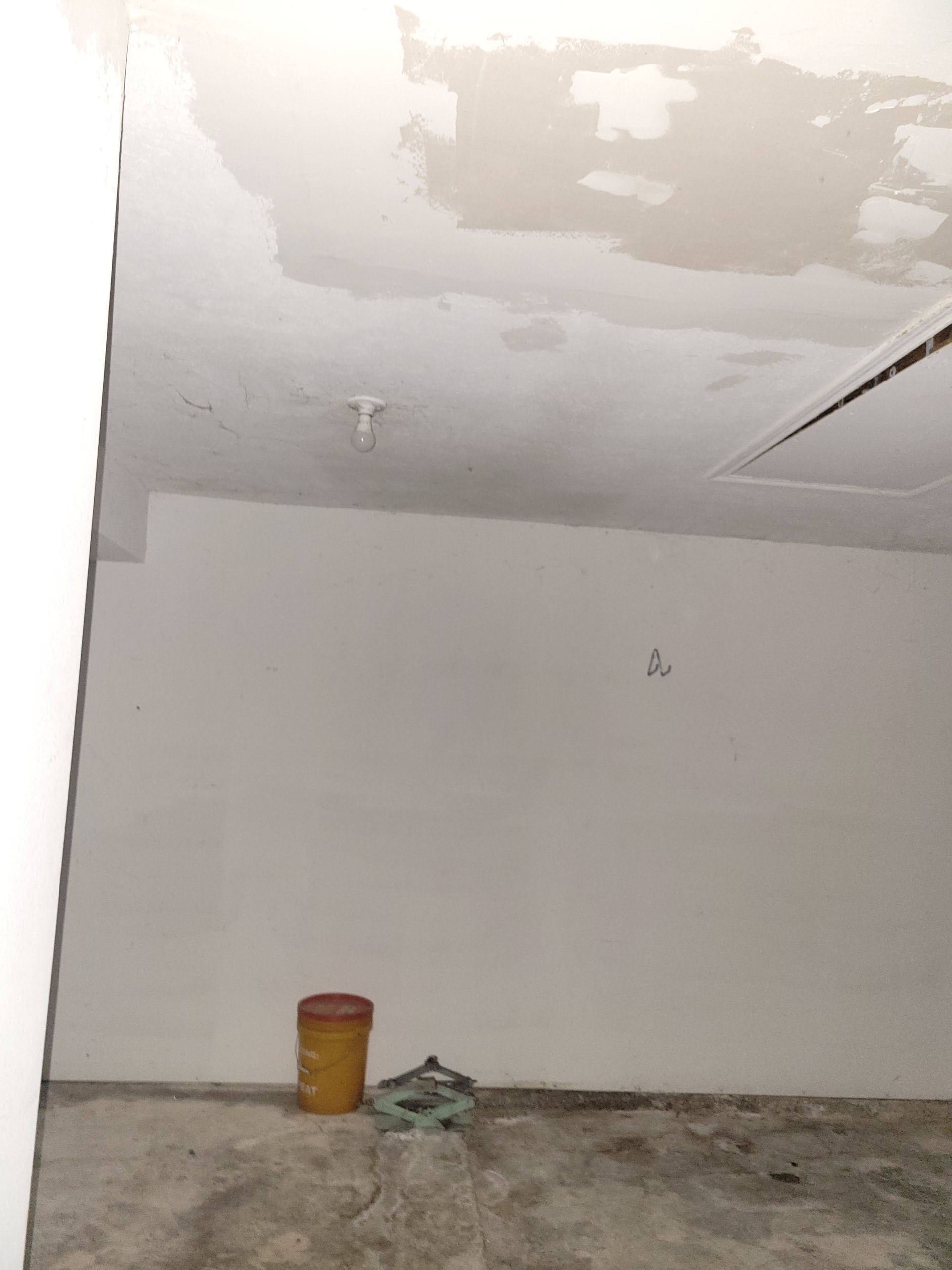 A room under renovation. White walls and ceiling, a bucket, and debris on the floor.