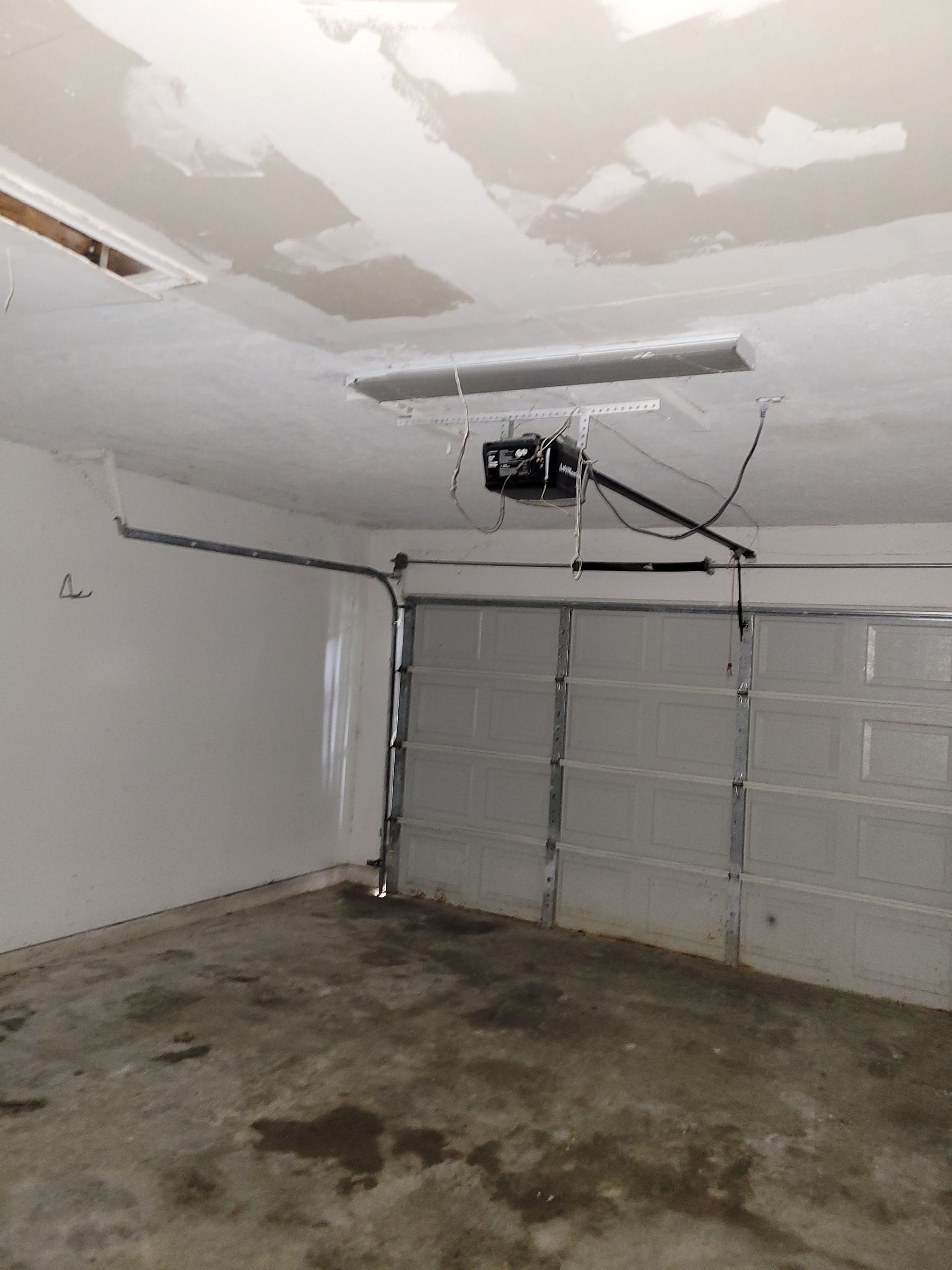 Garage interior with a closed garage door and a ceiling-mounted garage door opener.