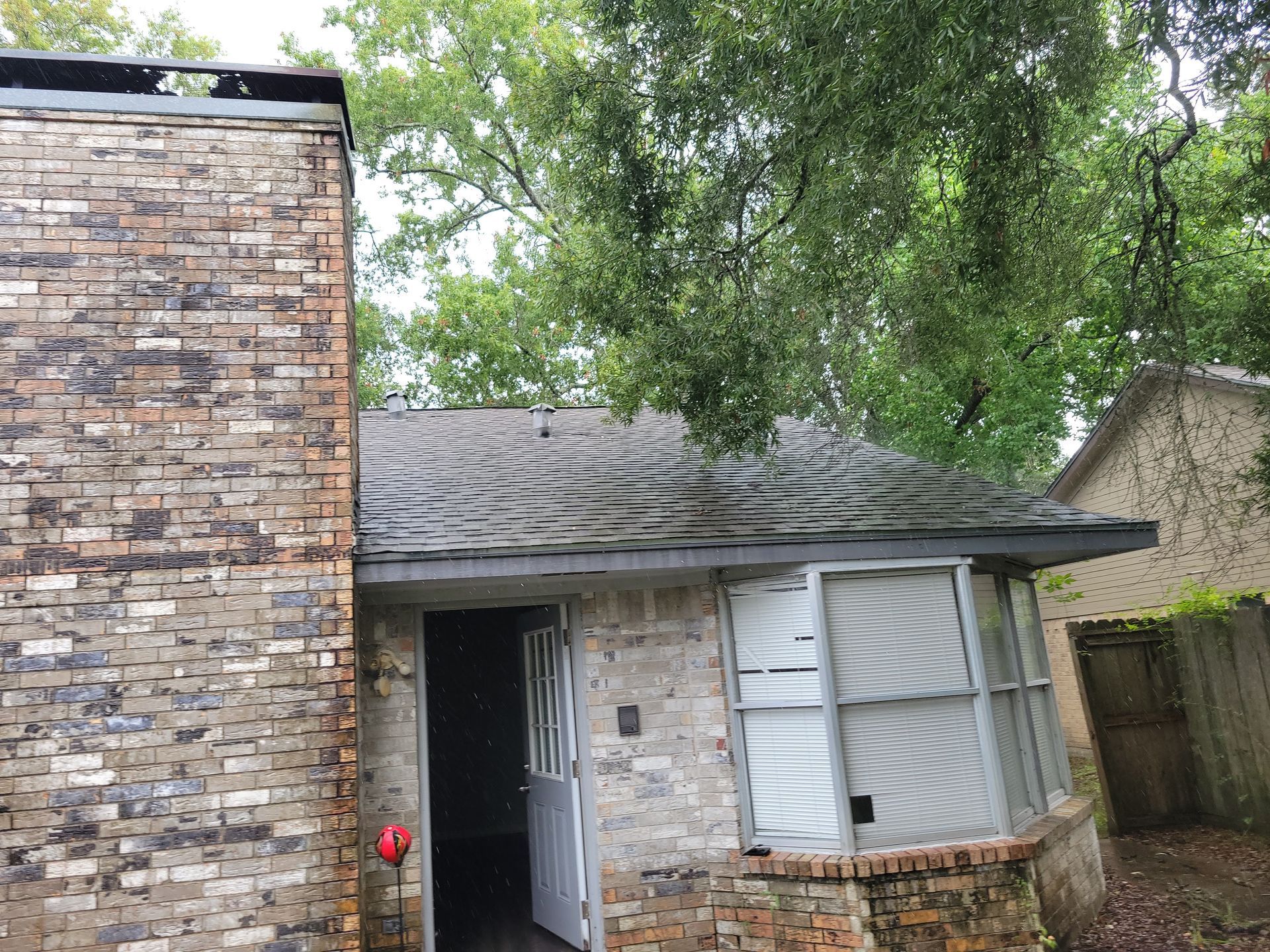 Brick building with a chimney, open door, and weathered roof. Trees in the background.
