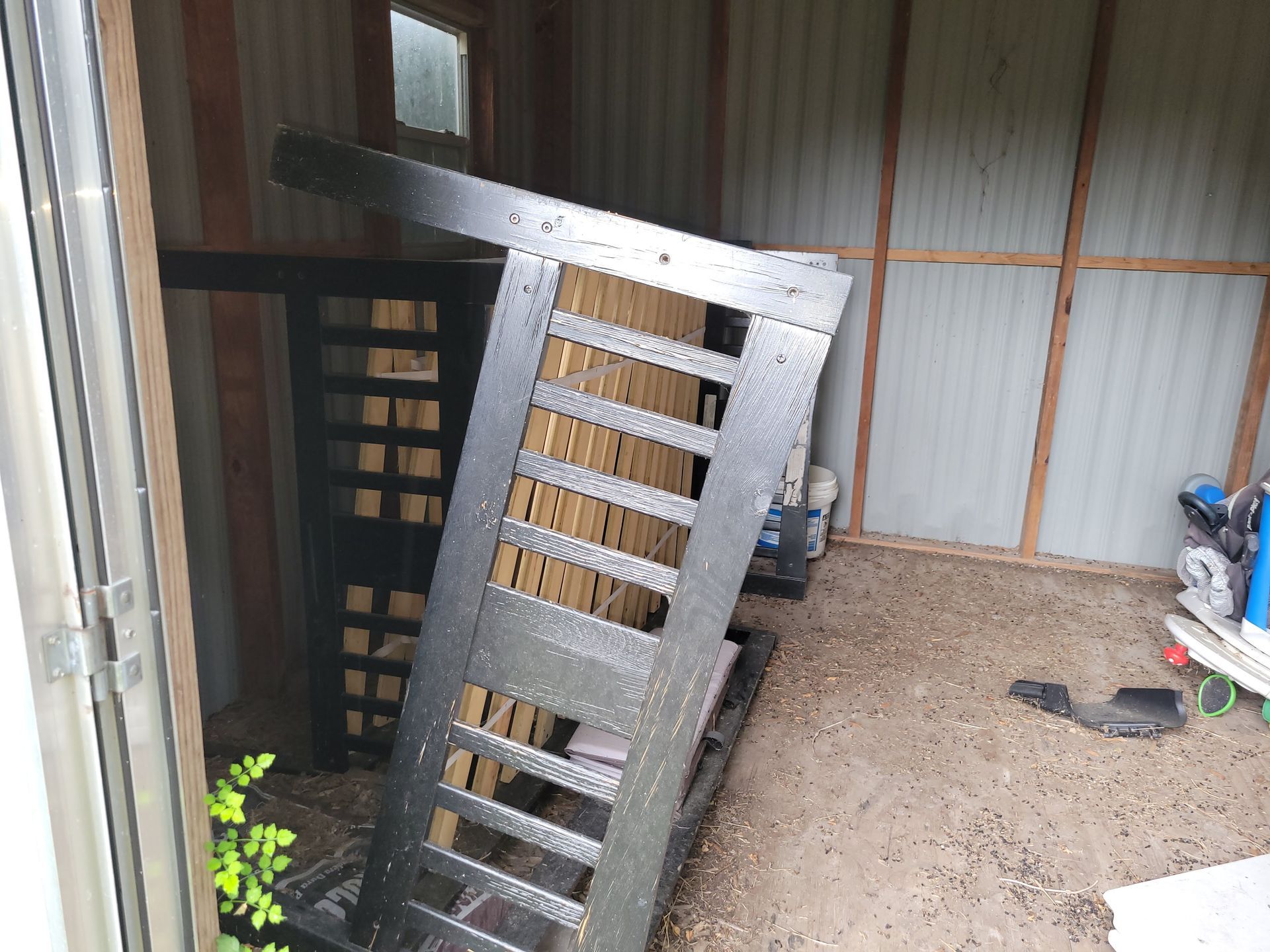 Black gate frame leaning against a wall in a shed with a small window.