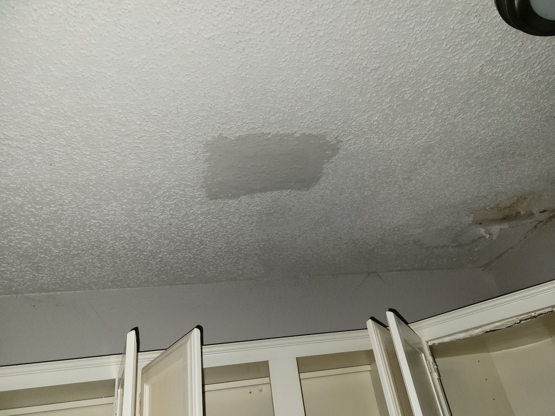 Water stain on a textured ceiling above a white cabinet.