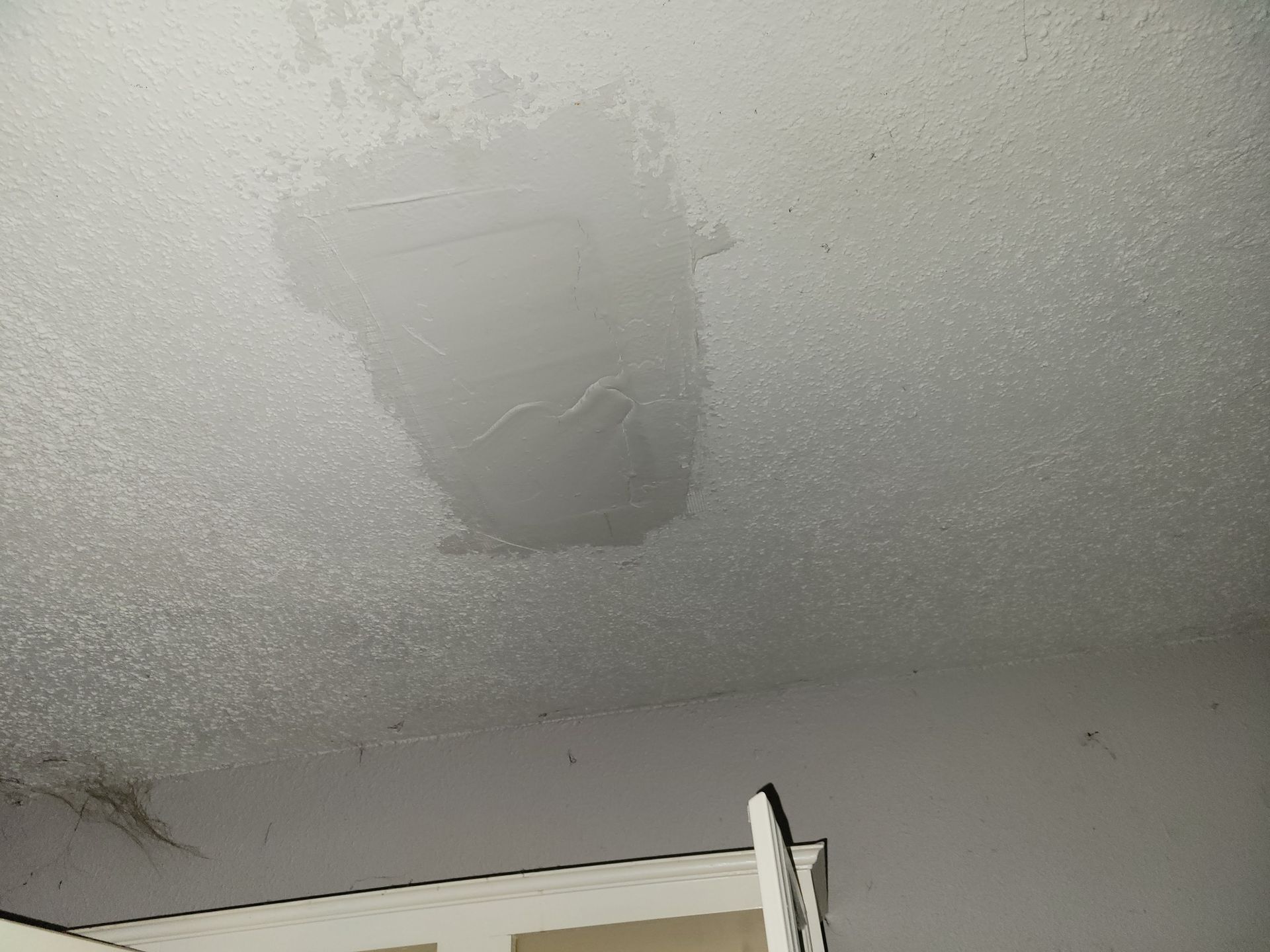 Patched section of a textured white ceiling with water damage and repaired area.