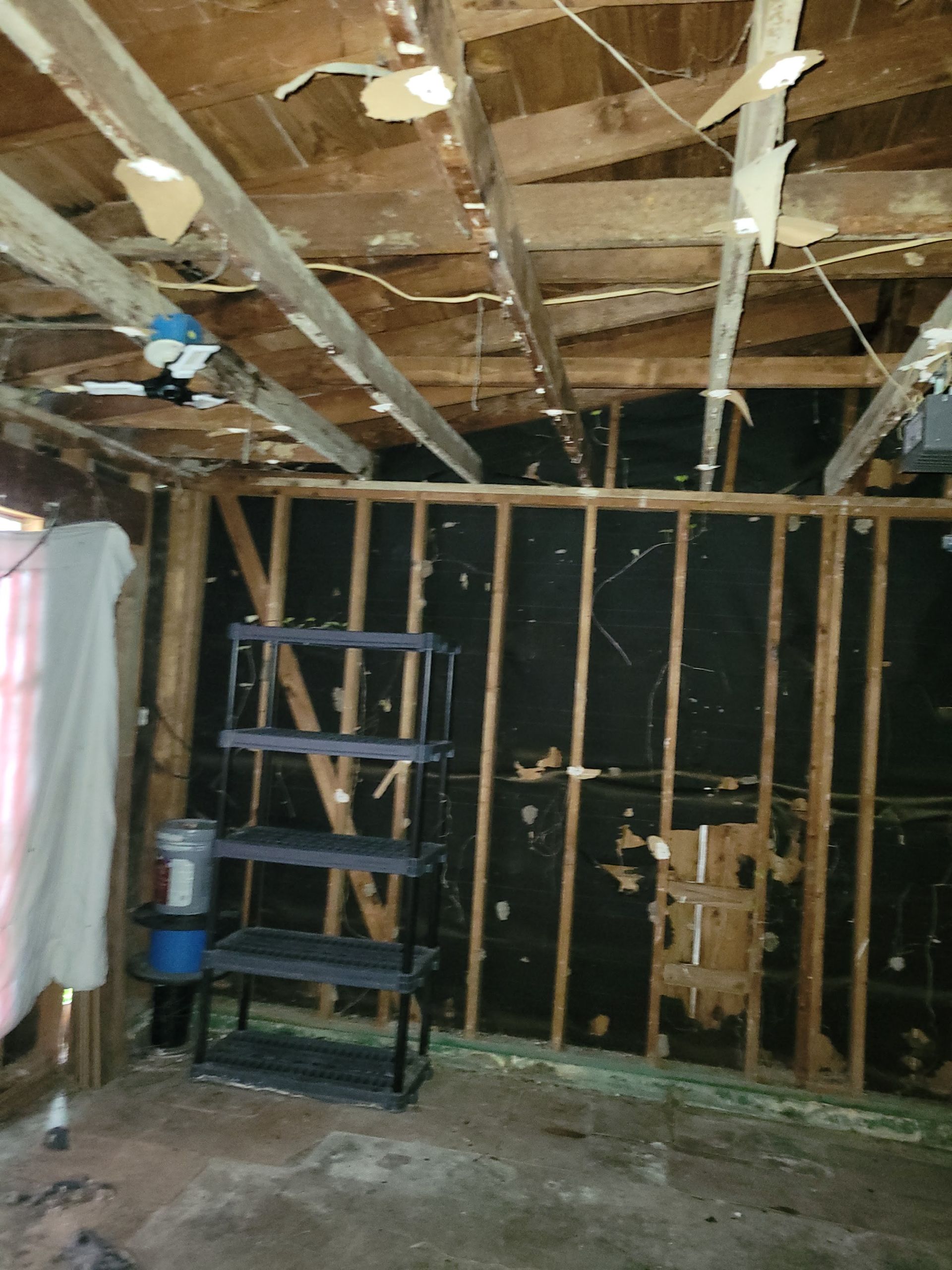 Interior of a room with exposed wooden ceiling beams, walls with black covering, and a plastic shelf unit.