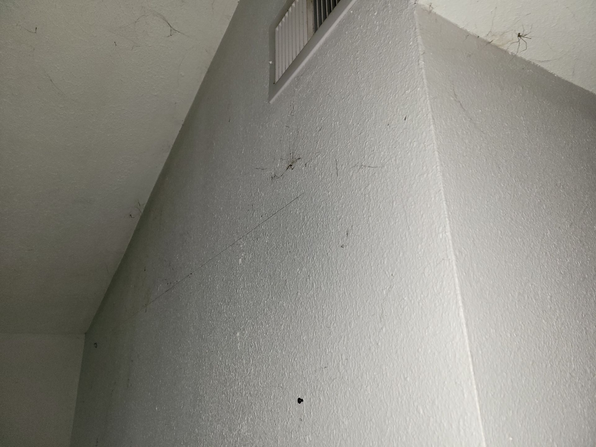 White textured walls and ceiling corner with air vent.