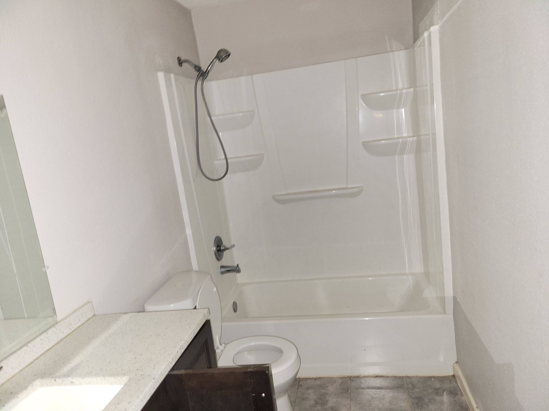 Bathroom with white tub/shower combo, toilet, vanity, and gray walls.