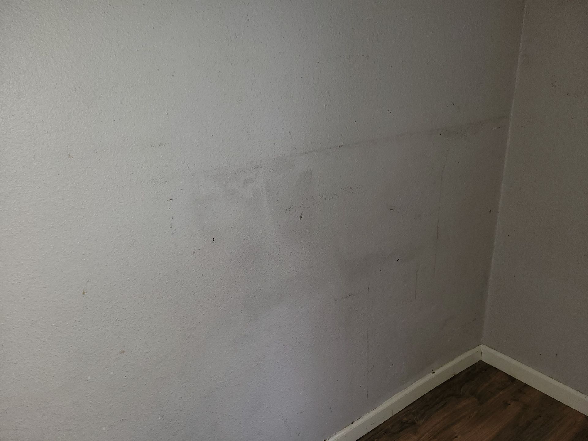 Gray interior walls show water damage near the corner of a room, with a wooden floor visible.