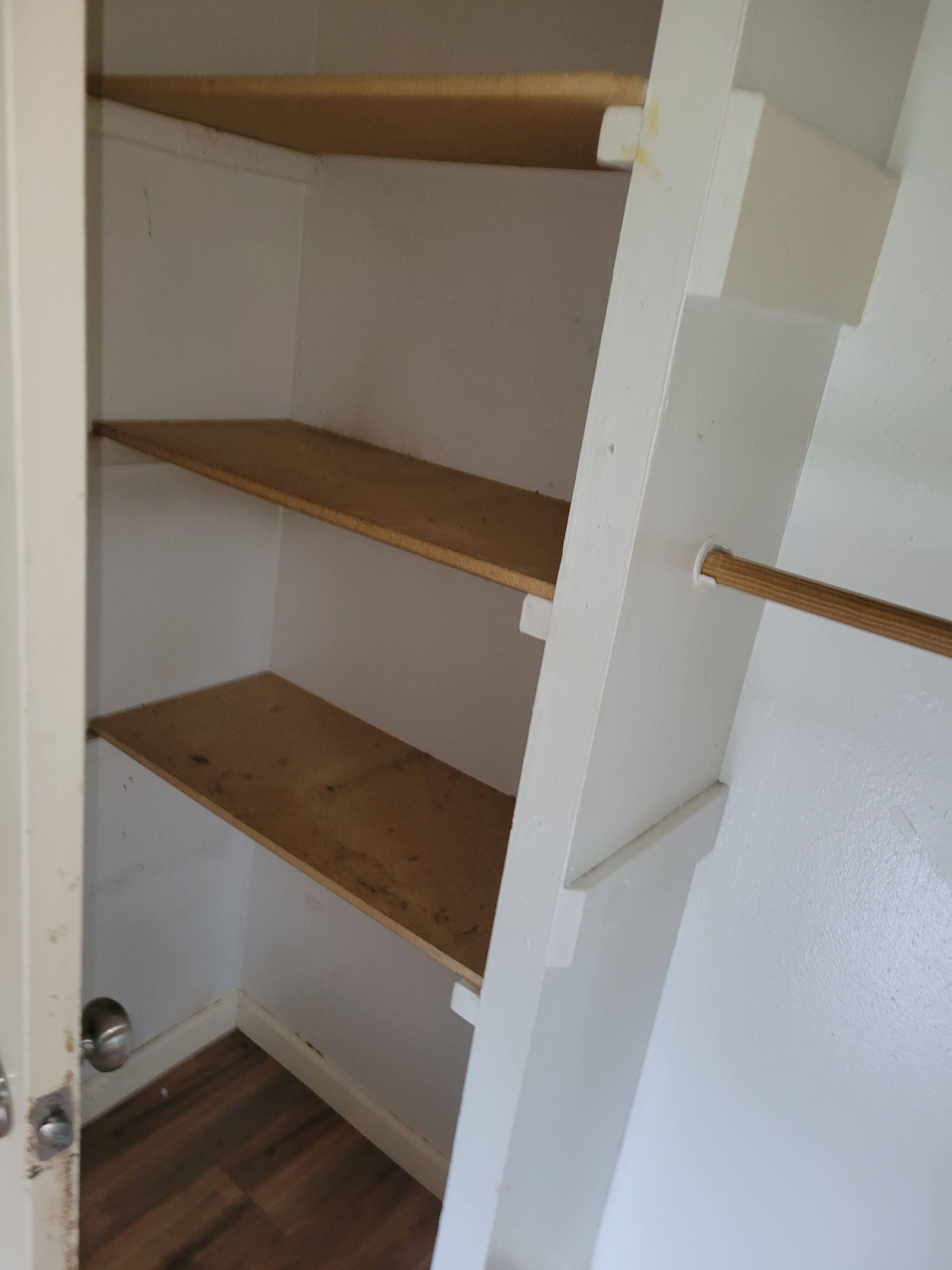 Empty white closet with wooden shelves and a hanging rod.