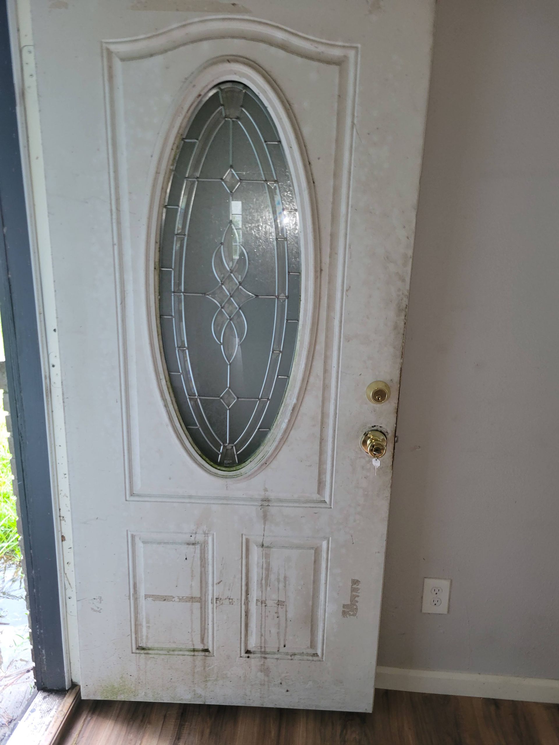 White exterior door with oval glass, dirty with stains.