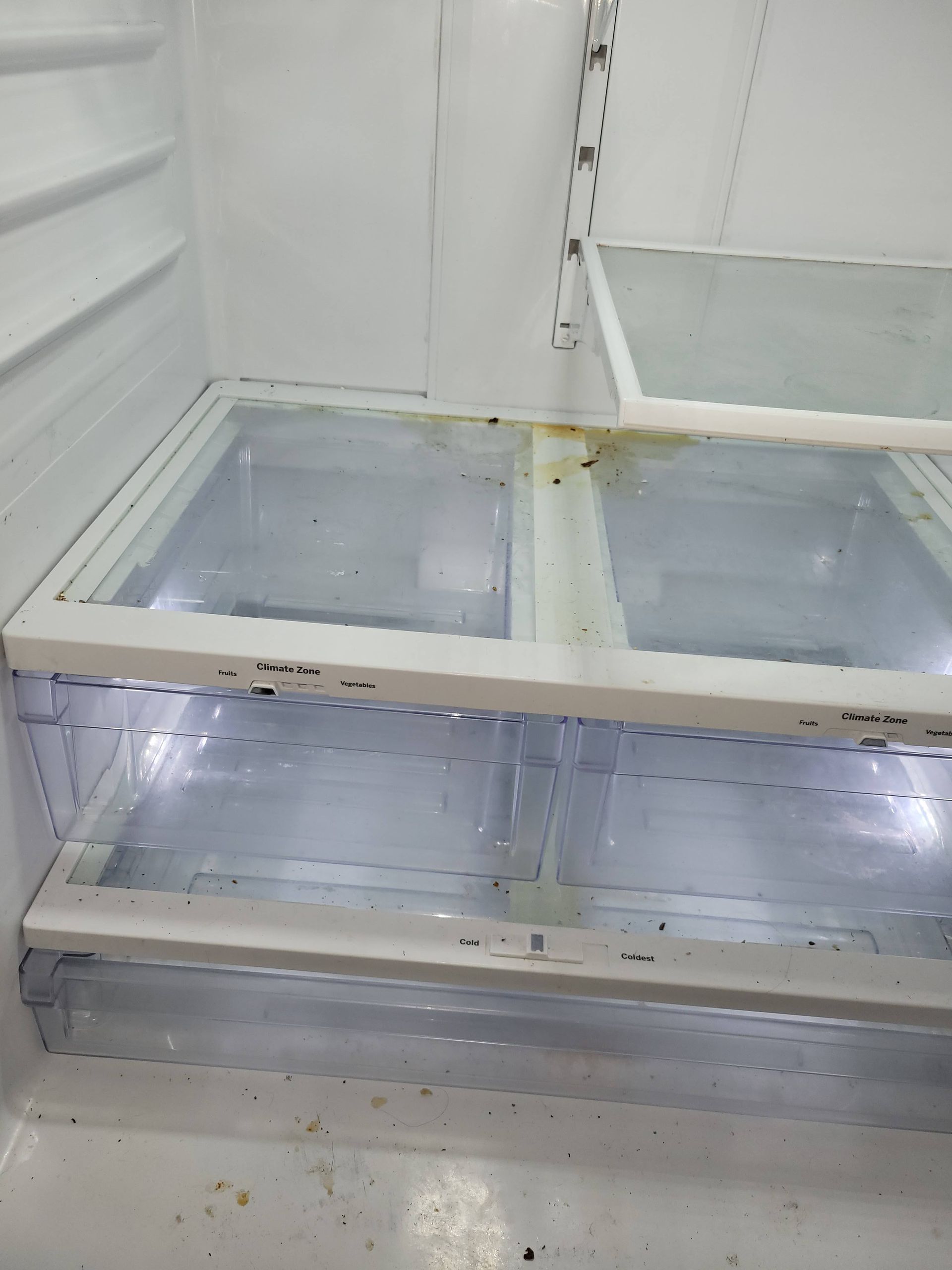 Inside of a white refrigerator, with clear plastic drawers and some visible mold.