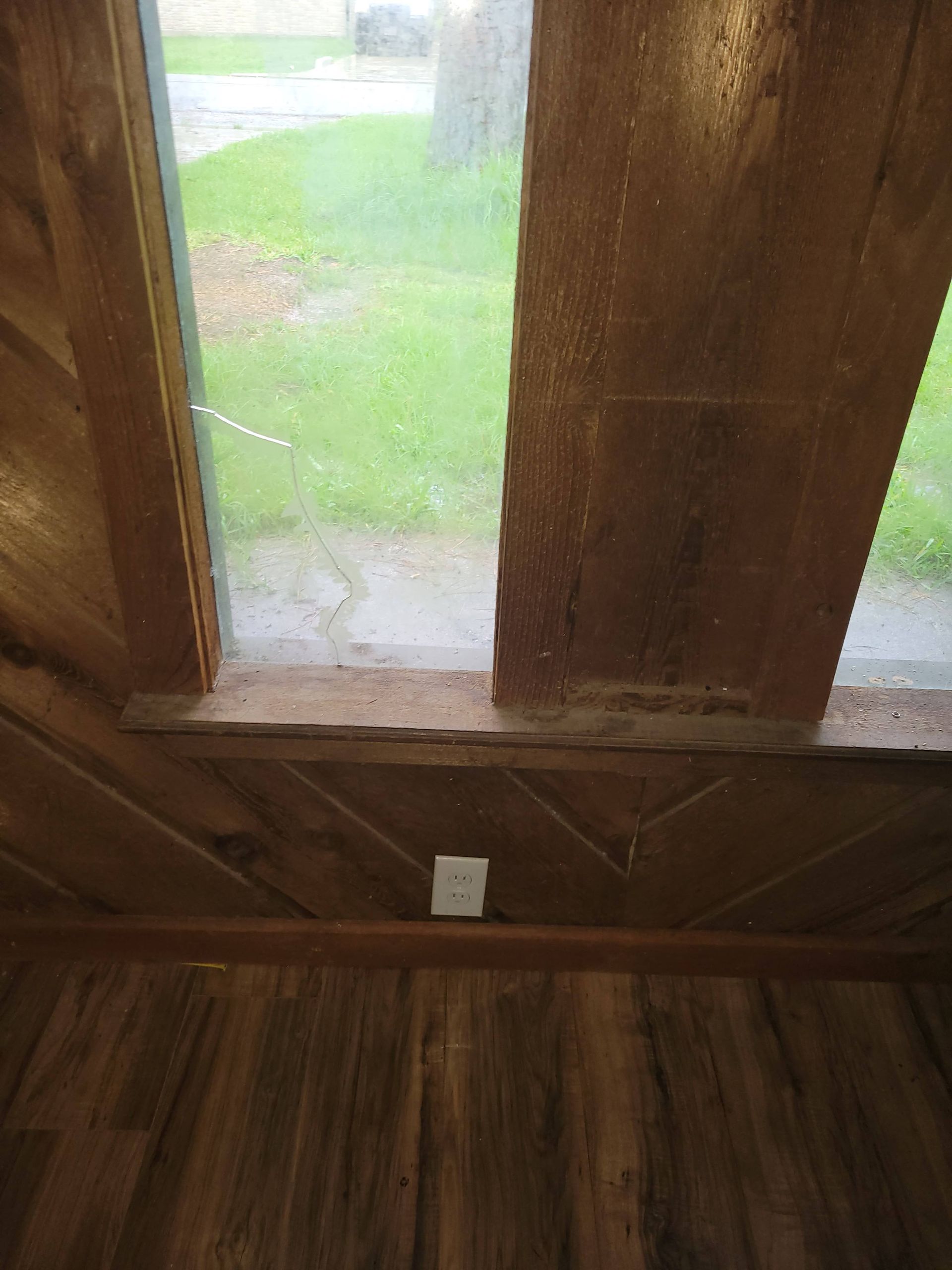 Interior view: wooden window frame with glass pane, power outlet, wood paneled wall and flooring.