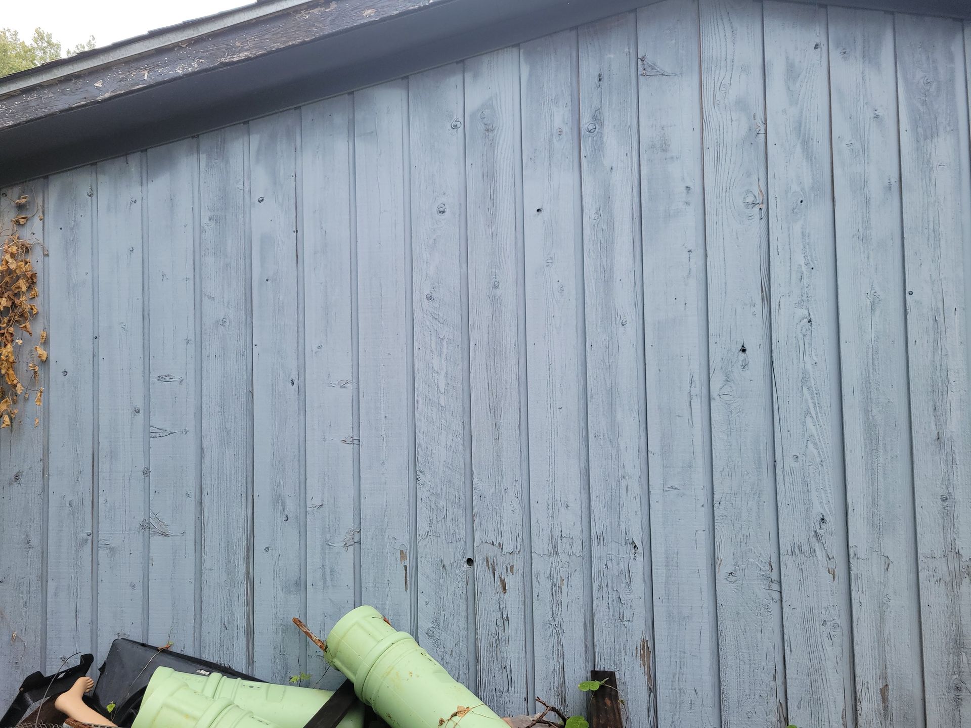 Weathered, blue wooden siding on a building with debris in the foreground.