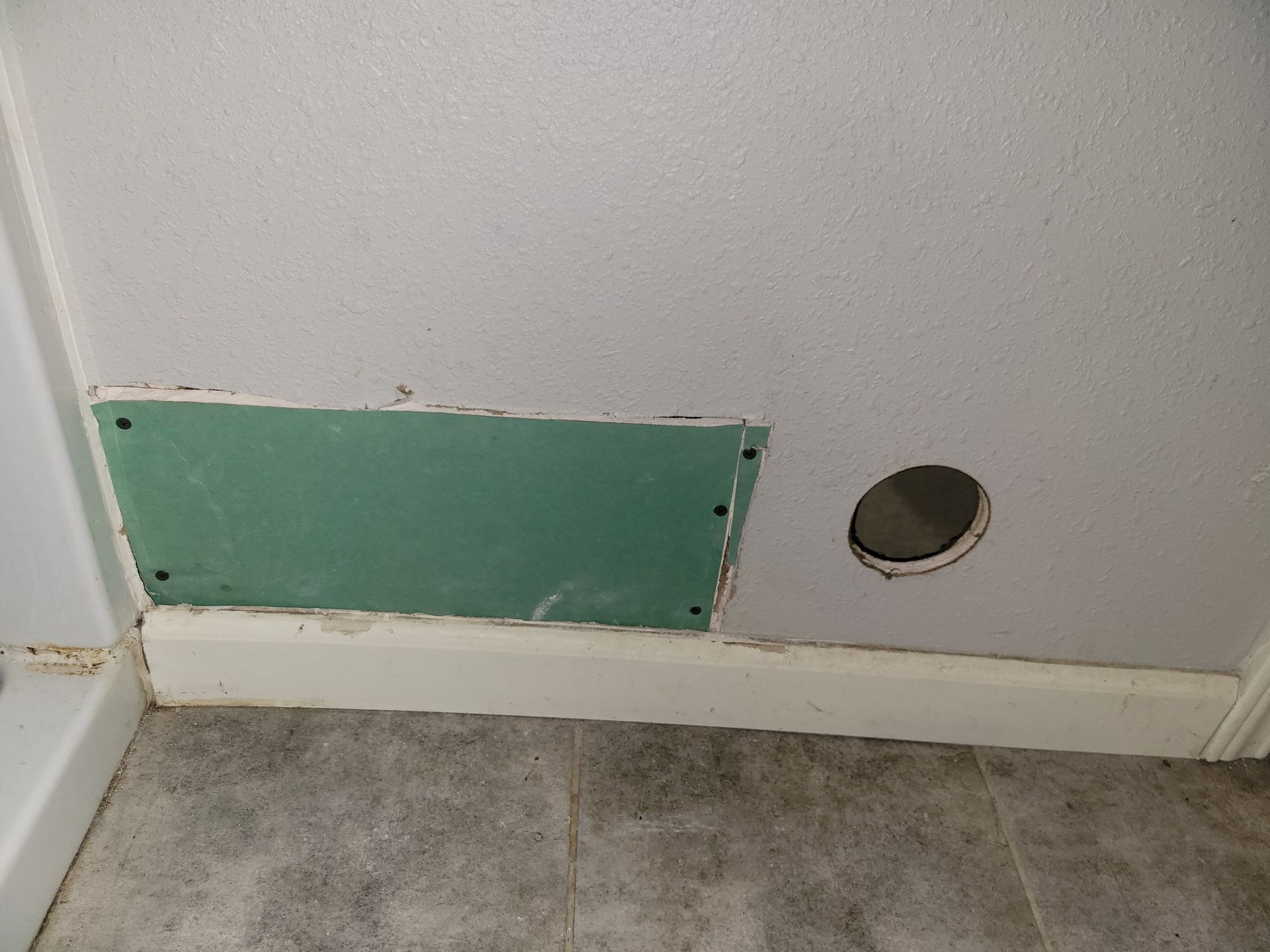 Green drywall patch on wall with a hole and baseboard trim.