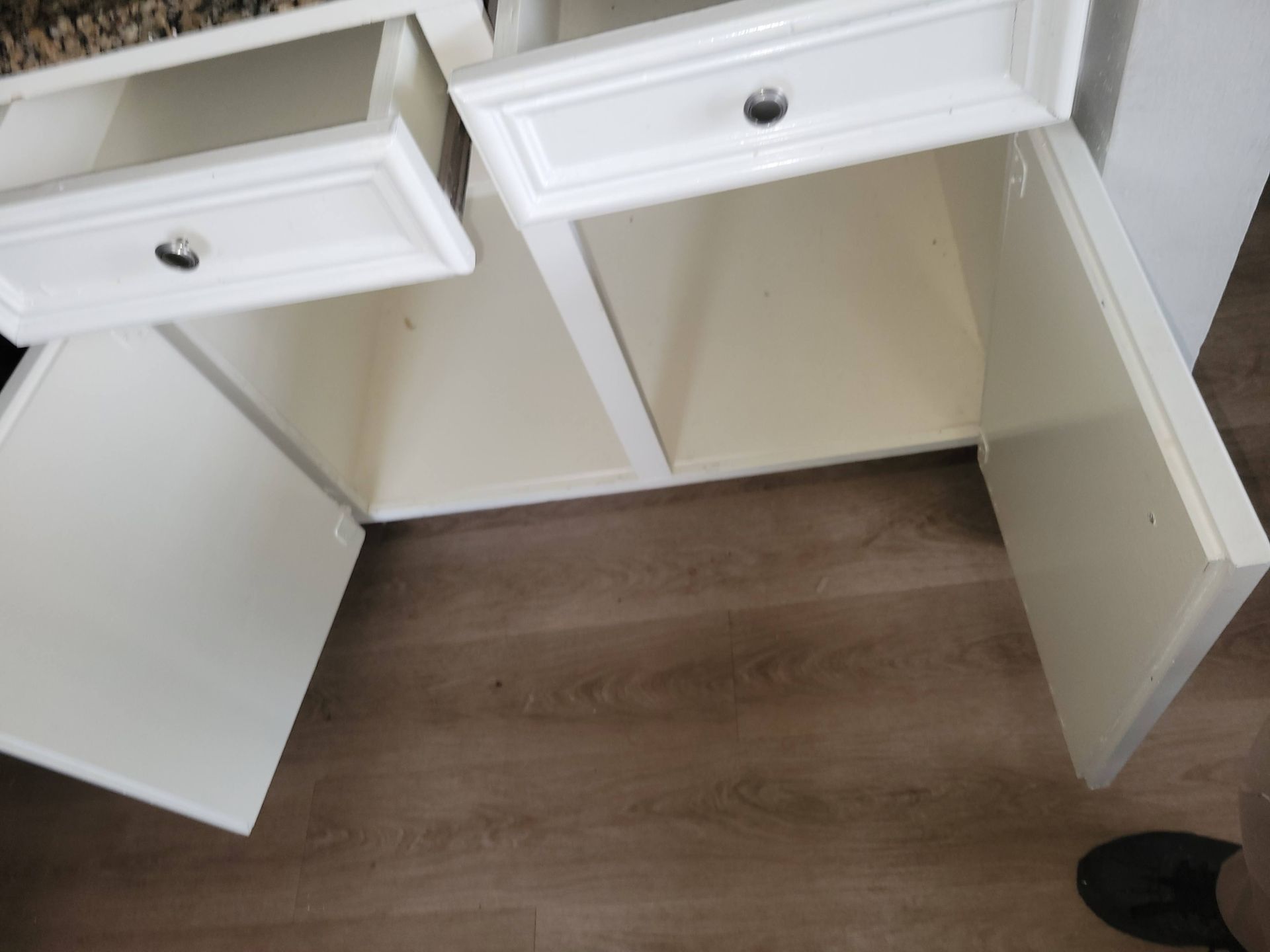 White vanity with open drawers and cabinet doors, on a wood floor.