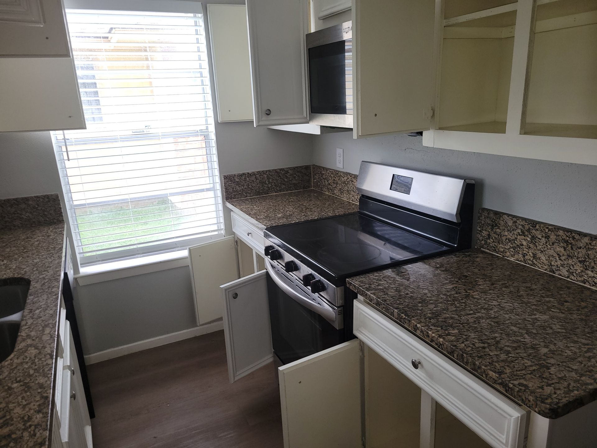 Kitchen with beige cabinets, granite countertops, and a stove next to an open window with blinds.