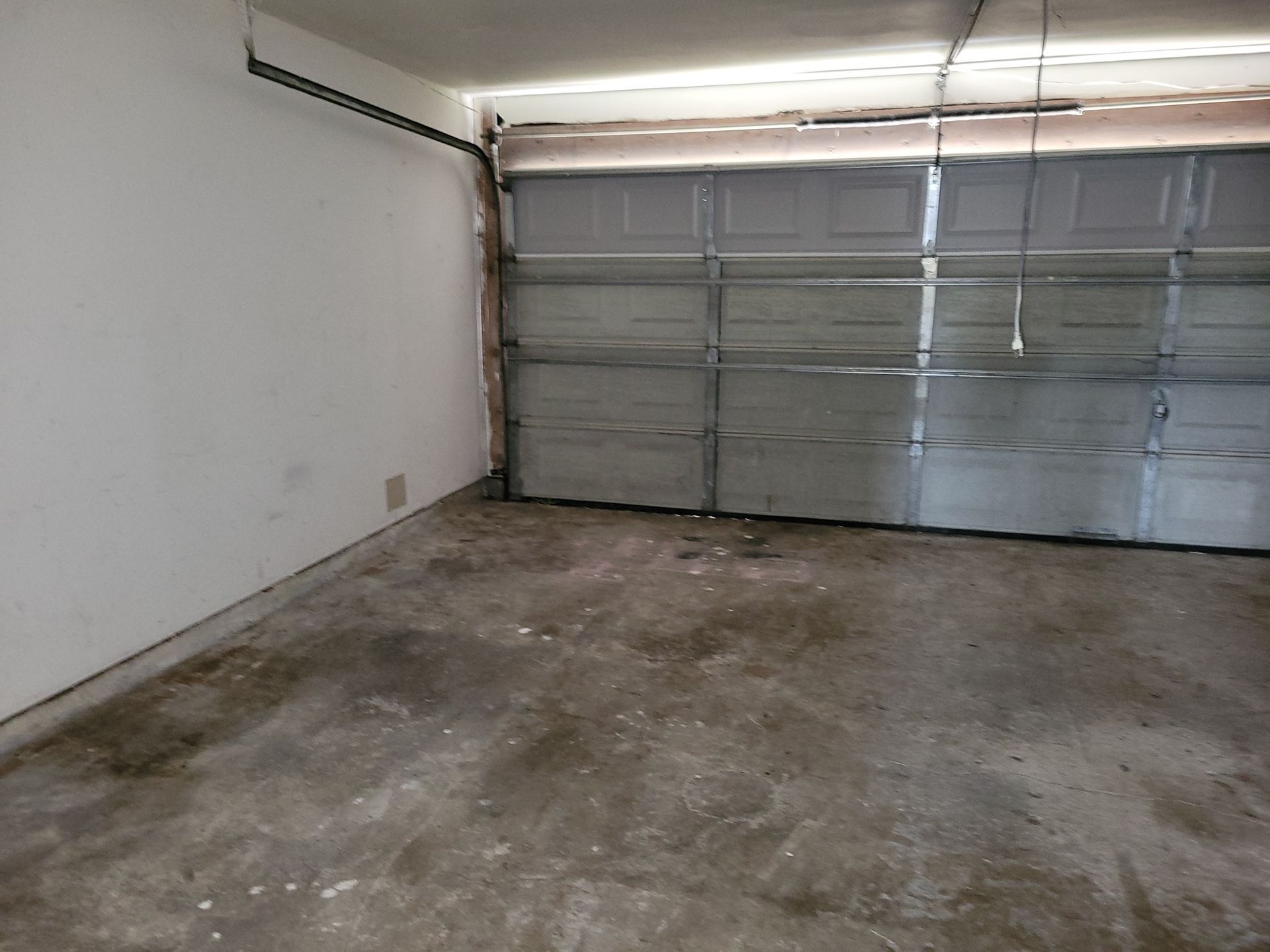 Empty, dirty garage interior with a closed gray garage door. White wall to the left, concrete floor.