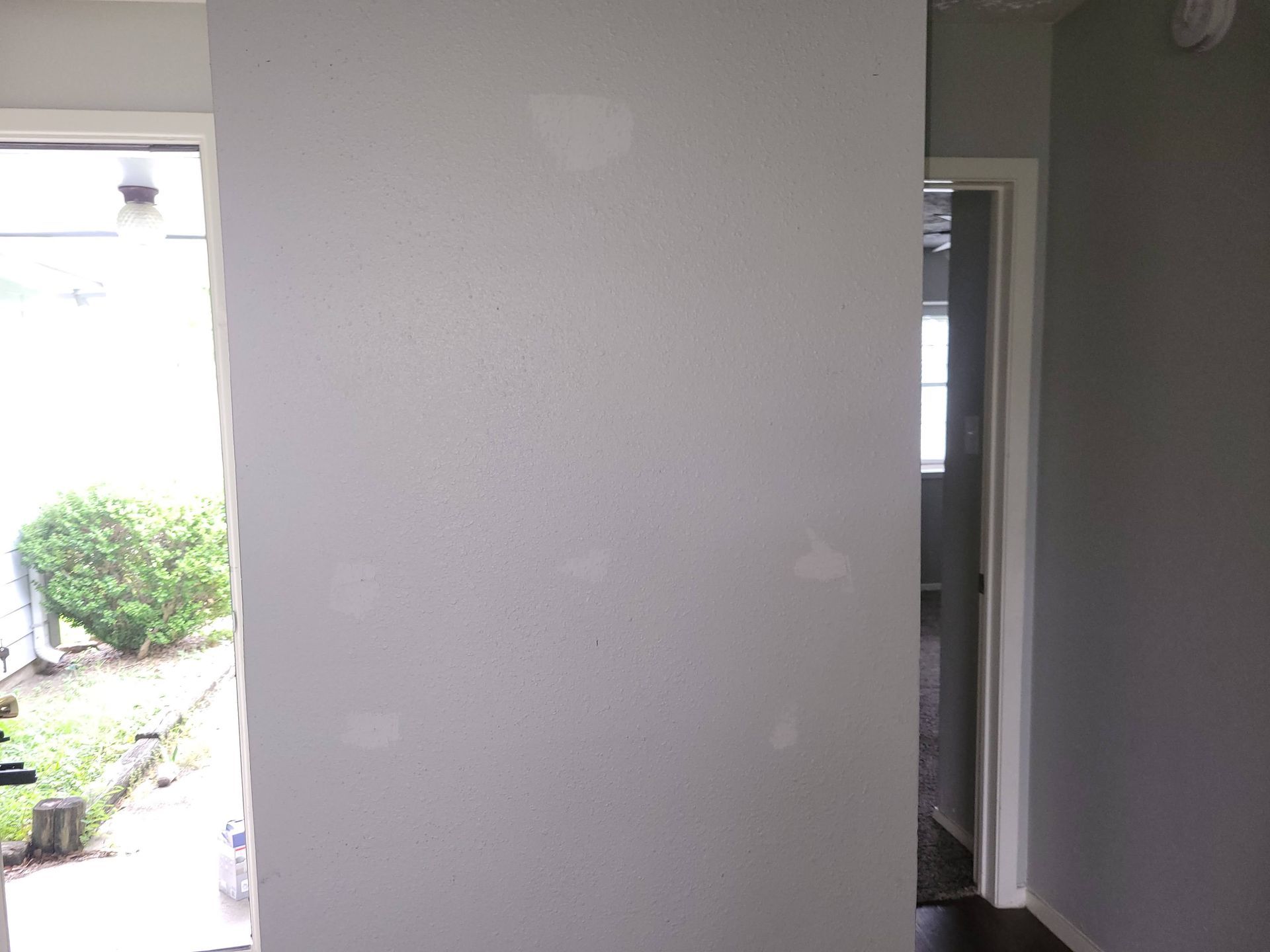White interior wall with patched areas, doorway on each side, one leading outside.