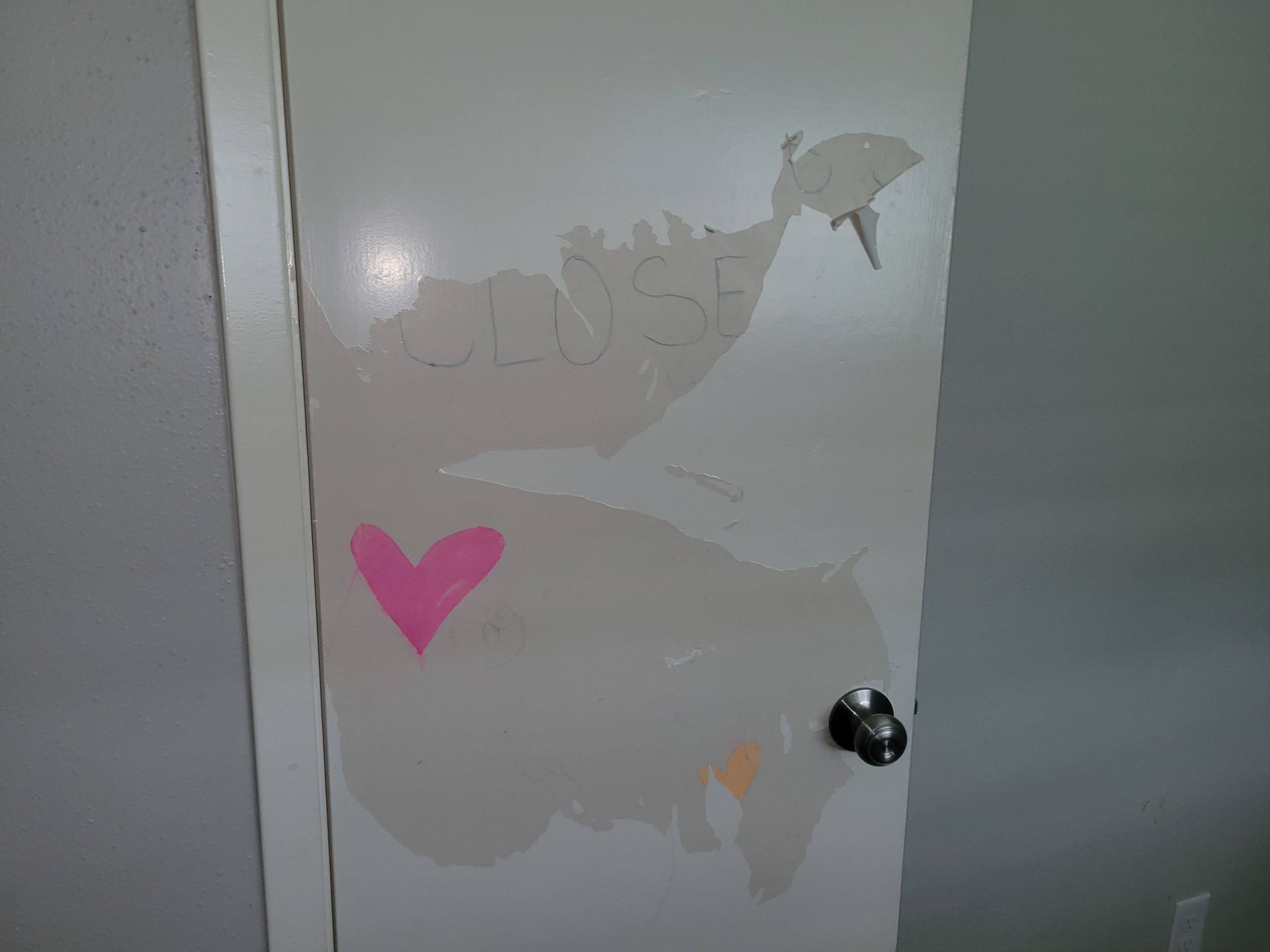 White door with chipped paint, a pink heart, and a doorknob.
