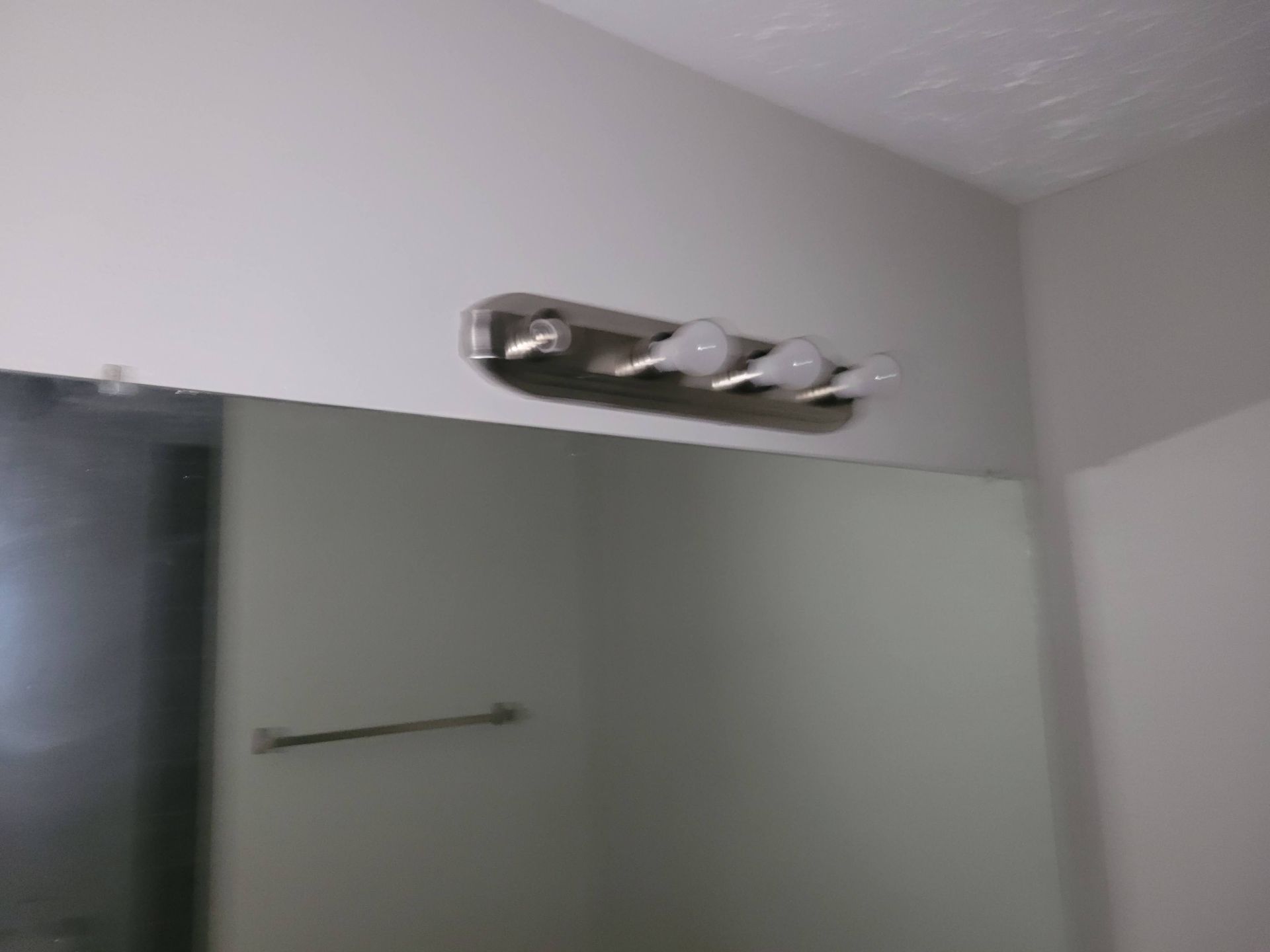 Bathroom mirror with a three-light vanity fixture above. A towel bar is below the mirror.