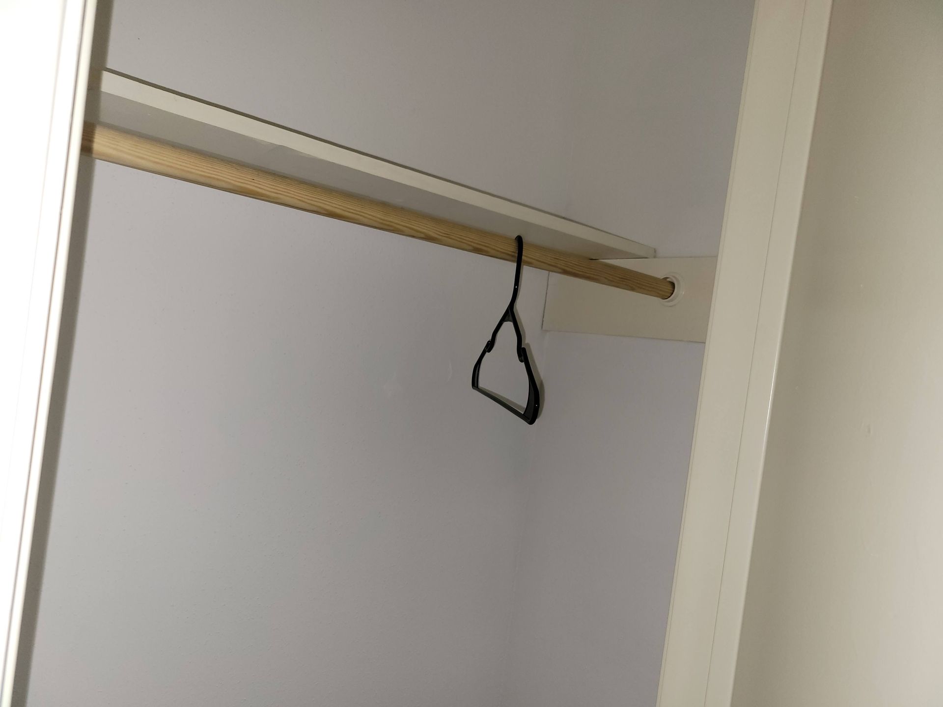 Empty white closet with a wooden rod and a black hanger.