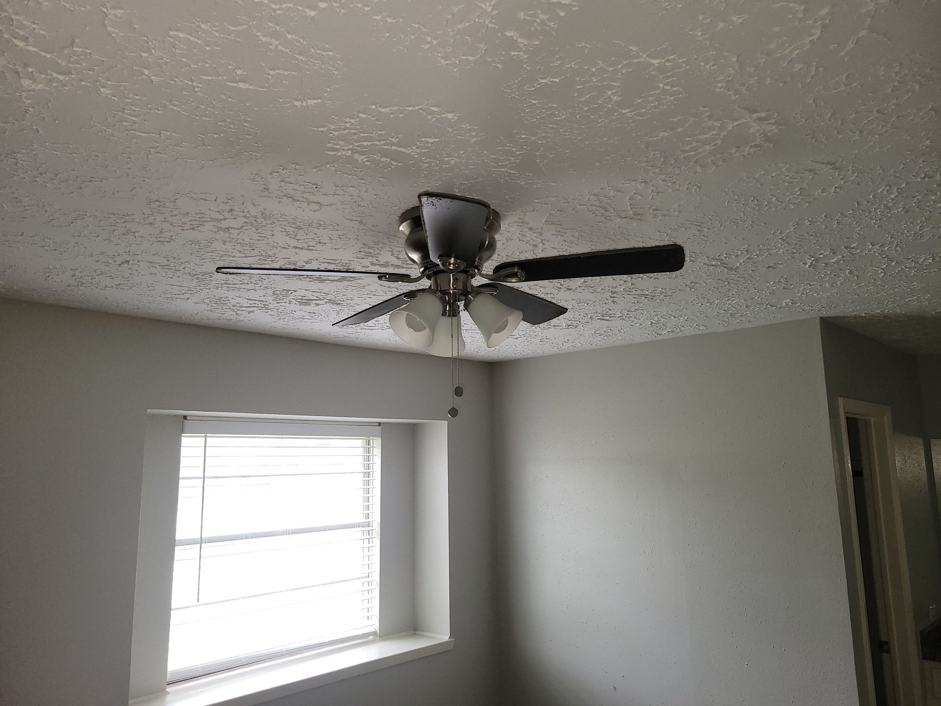 Ceiling fan with lights in a room with a window and white walls.