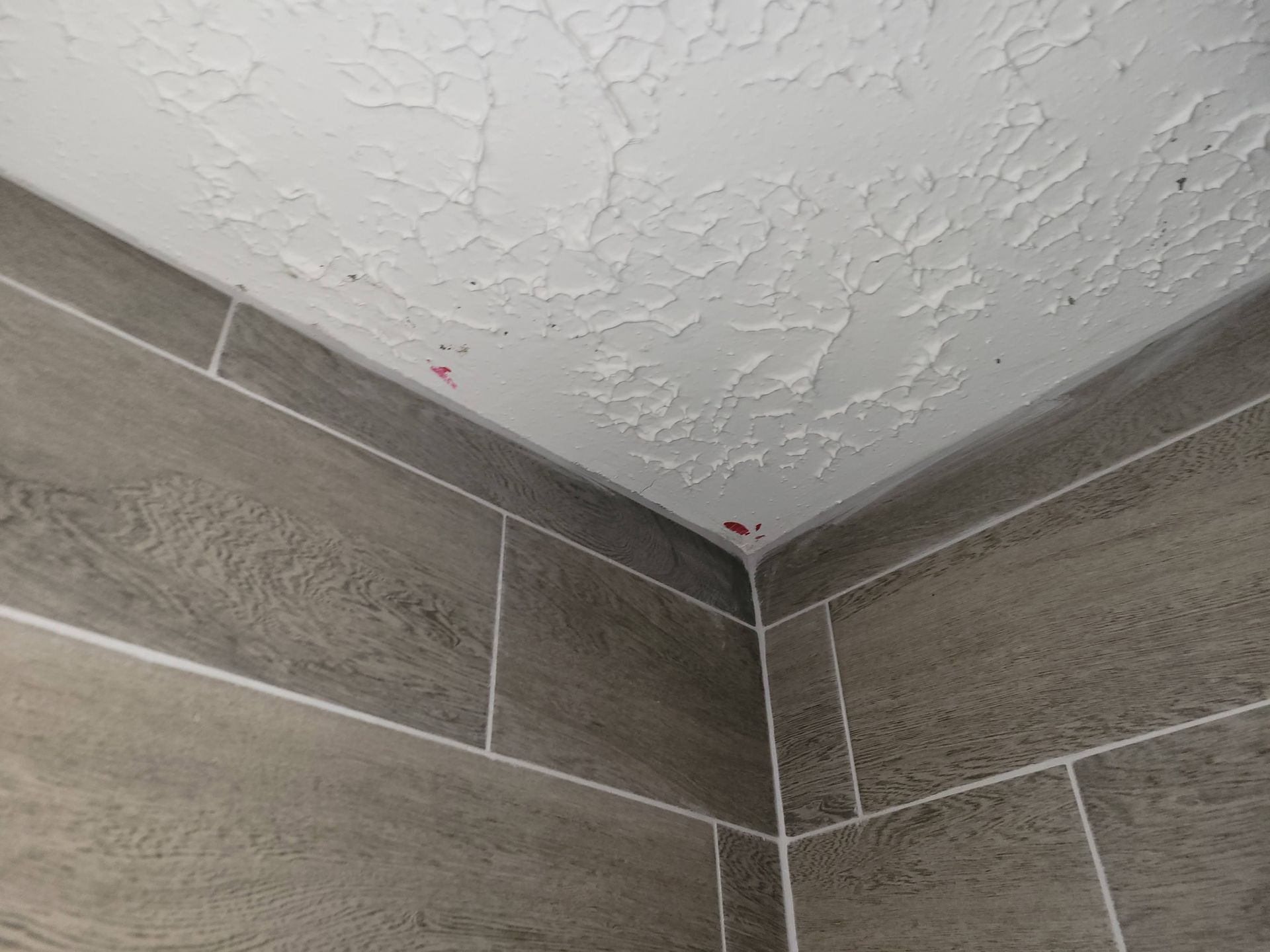 White peeling paint on bathroom ceiling corner, gray tiled walls.