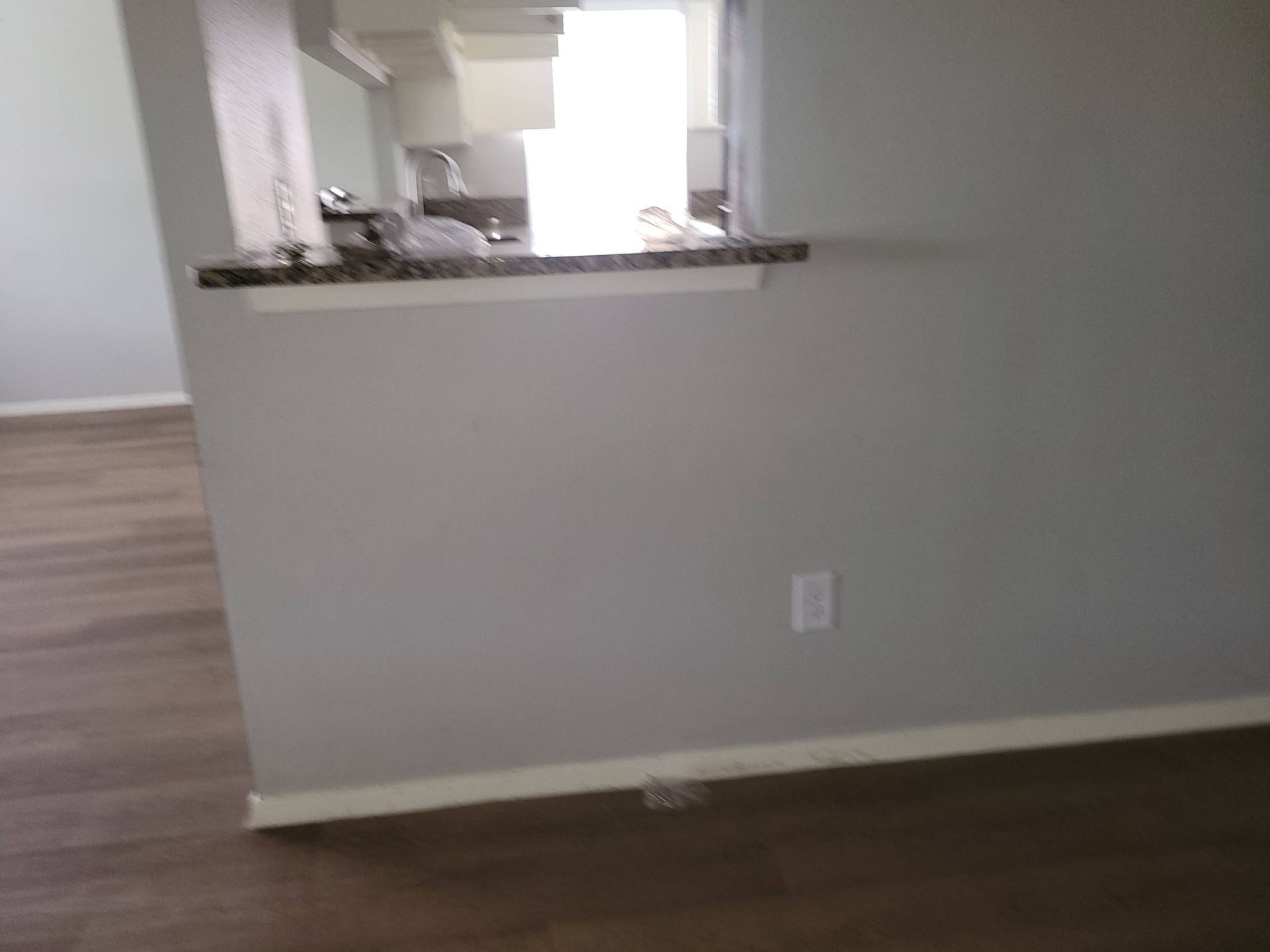 A room with grey walls and a dark wood floor, a countertop with an opening to a kitchen in the background.