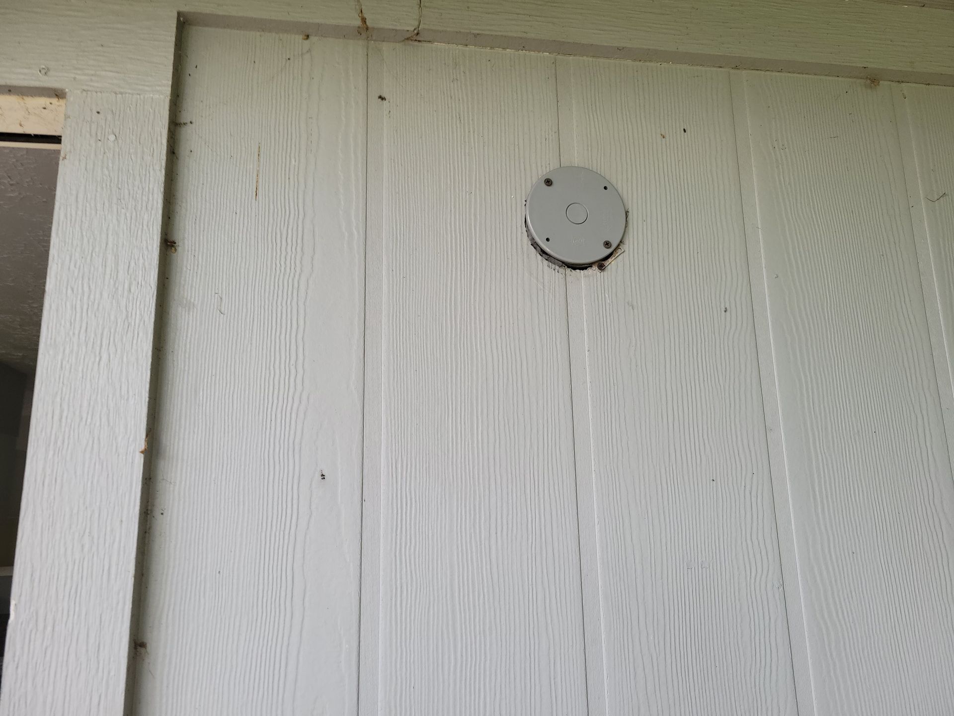 White siding with a circular, metal vent cover attached.