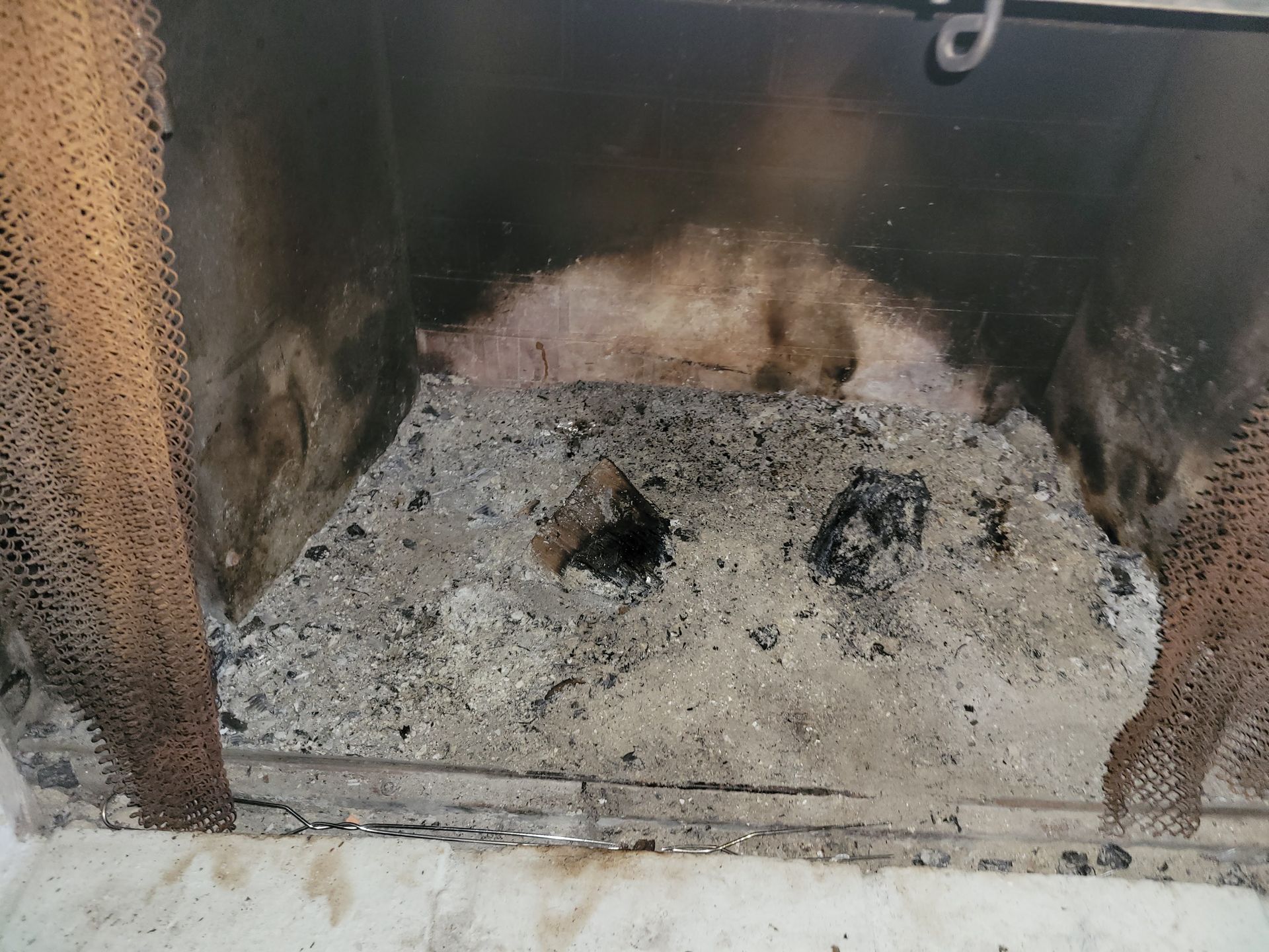 Fireplace interior with ash, soot, and remnants of burnt wood. Mesh screens on sides.