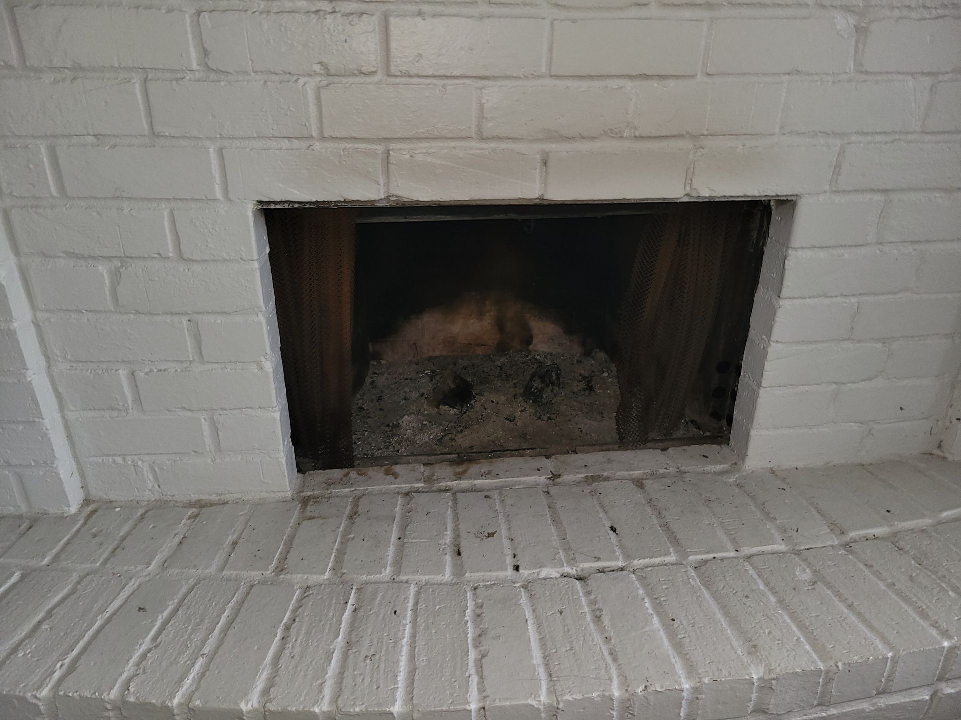 White painted brick fireplace, open interior, soot and wood visible.