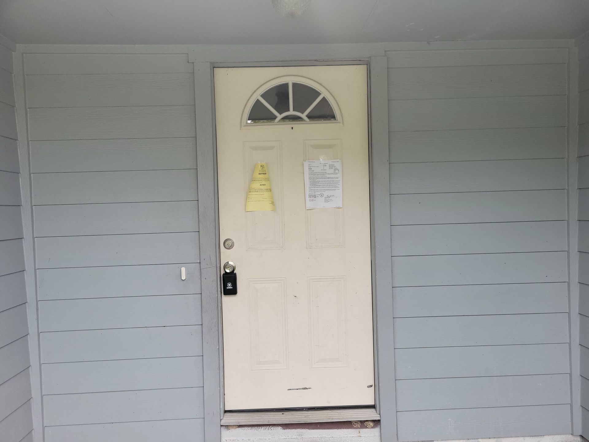 White door with arched window, gray siding, and a sign.