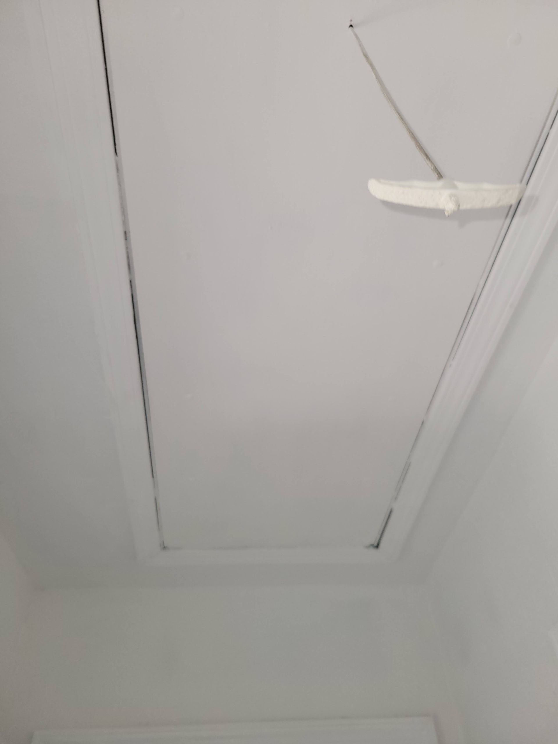 White ceiling with rectangular access panel outlined in black. A pull-down latch is visible.