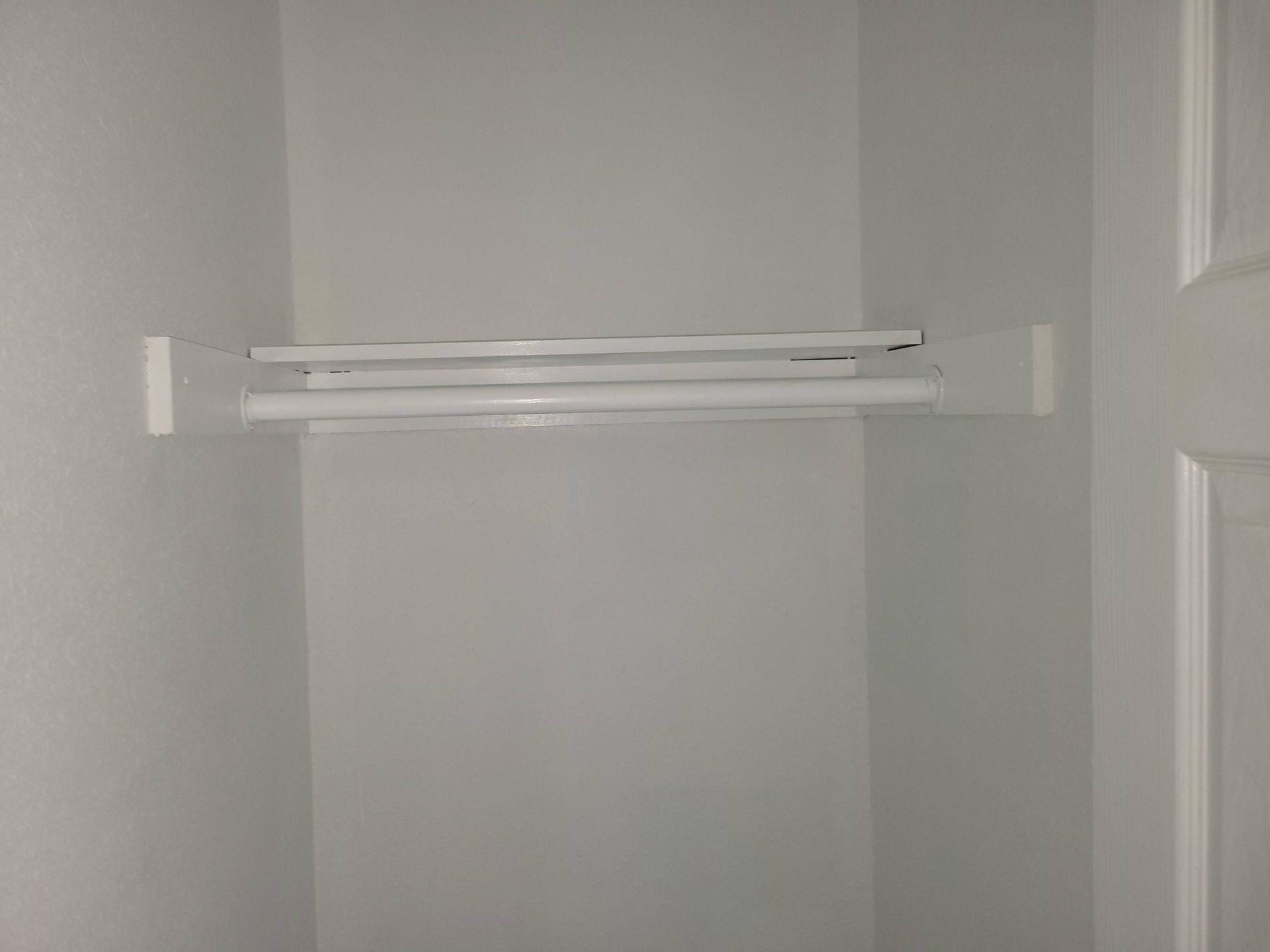 White closet interior with a shelf and hanging rods.