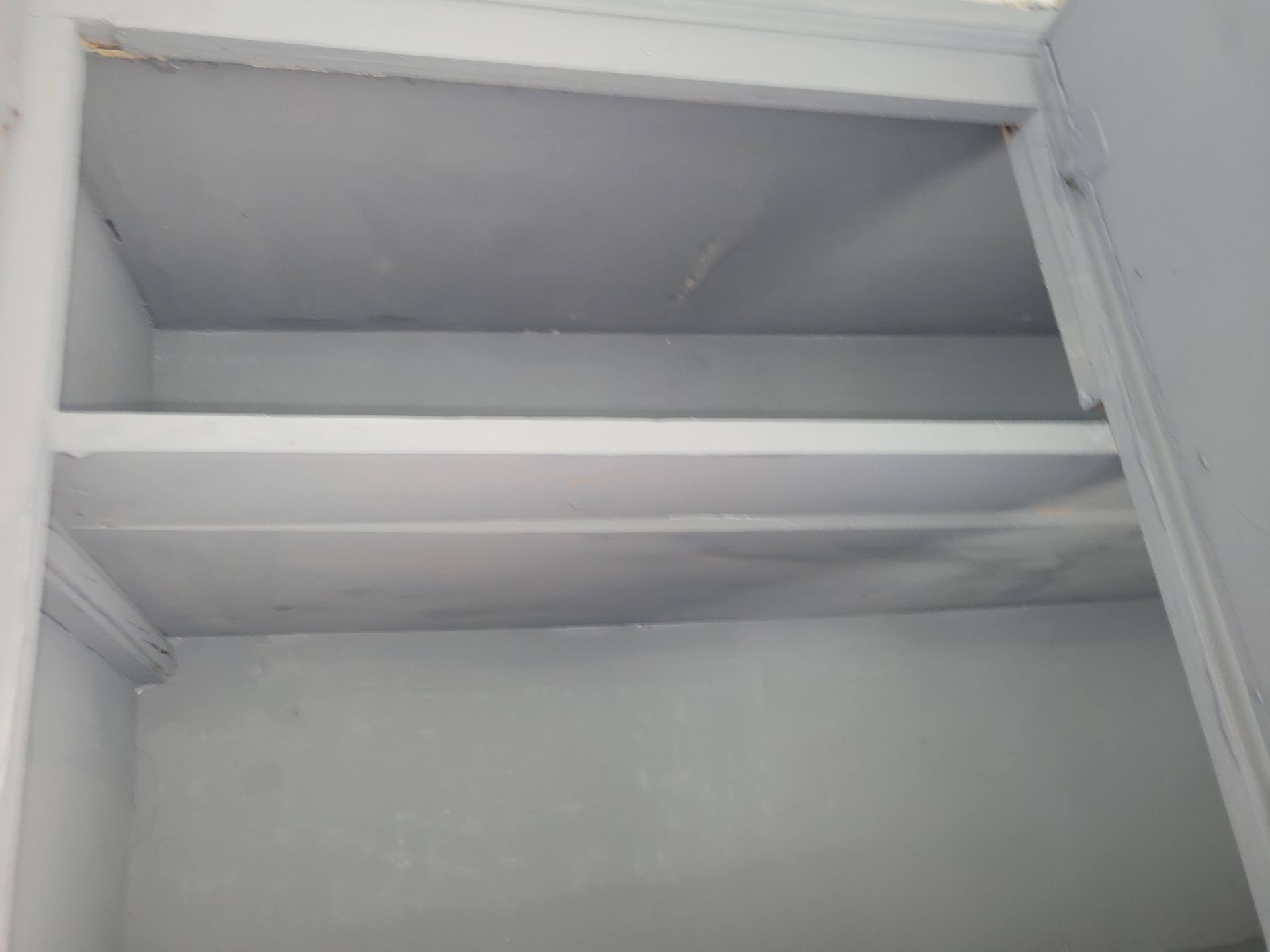 Empty gray-painted shelves inside a cabinet, viewed from a low angle.