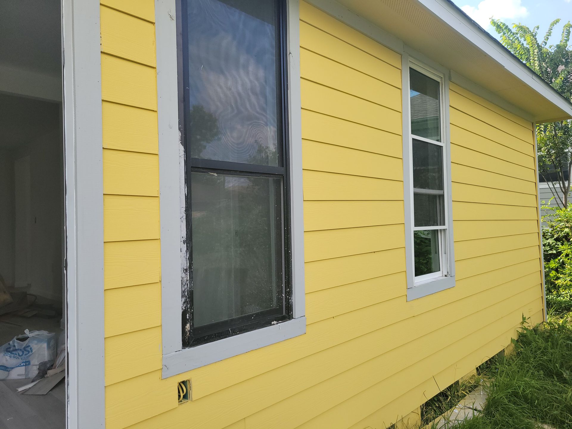 Yellow house with white-framed windows, weathered black window, and unfinished interior.