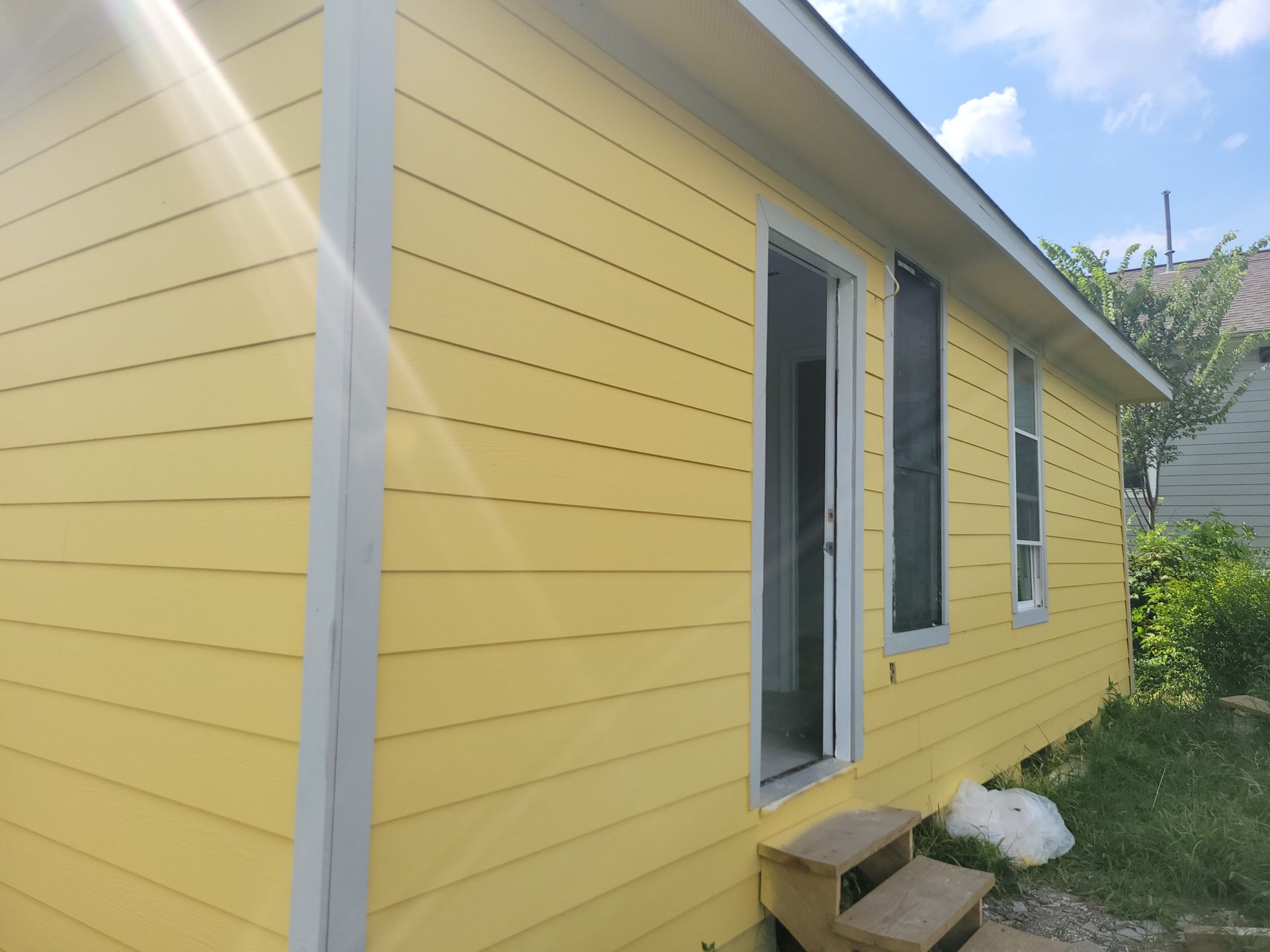 Yellow house with white trim, open door, two windows, two wooden steps.